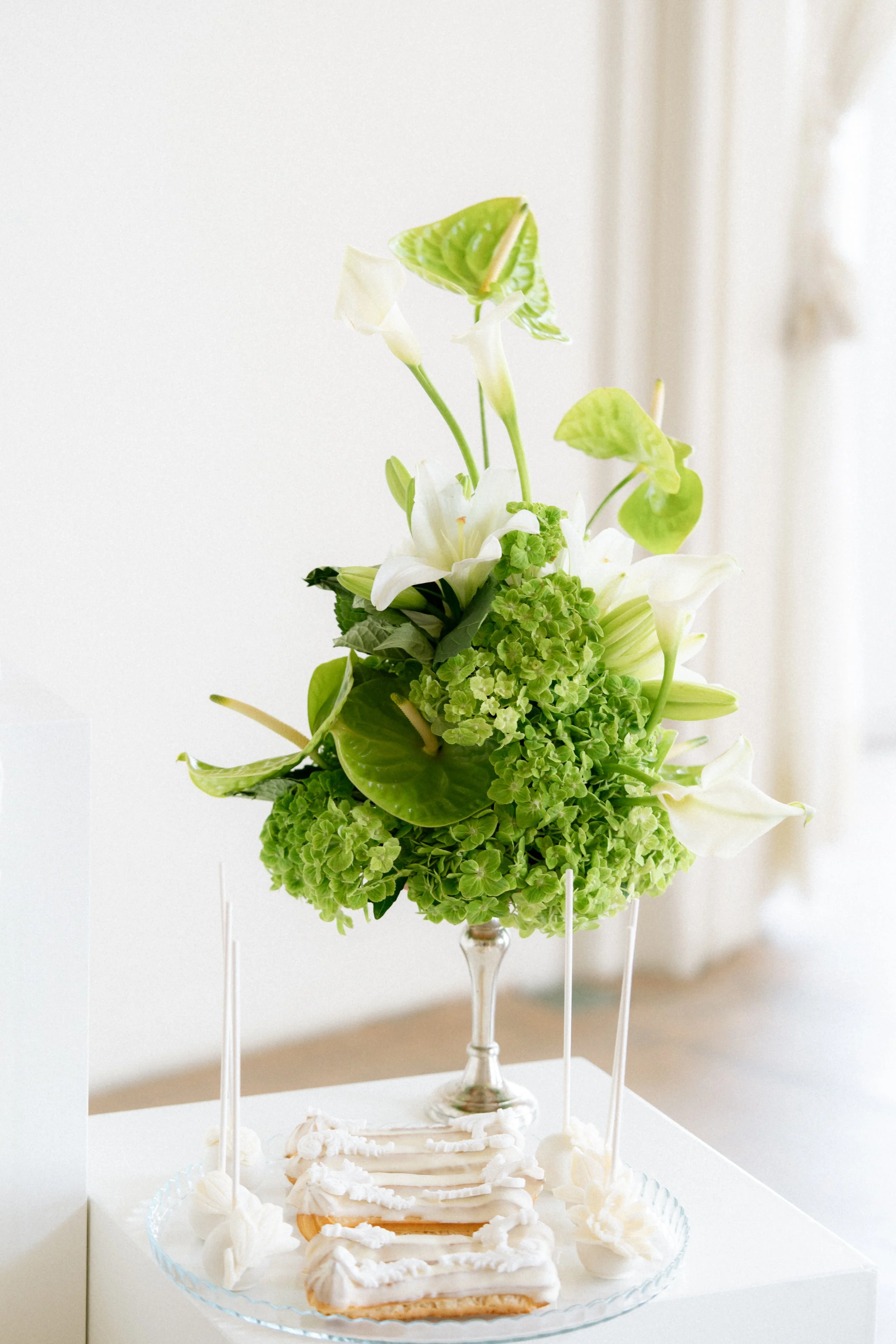 Eclairs und Macarons mit grüner Hochzeitsfloristik auf Dessertisch.