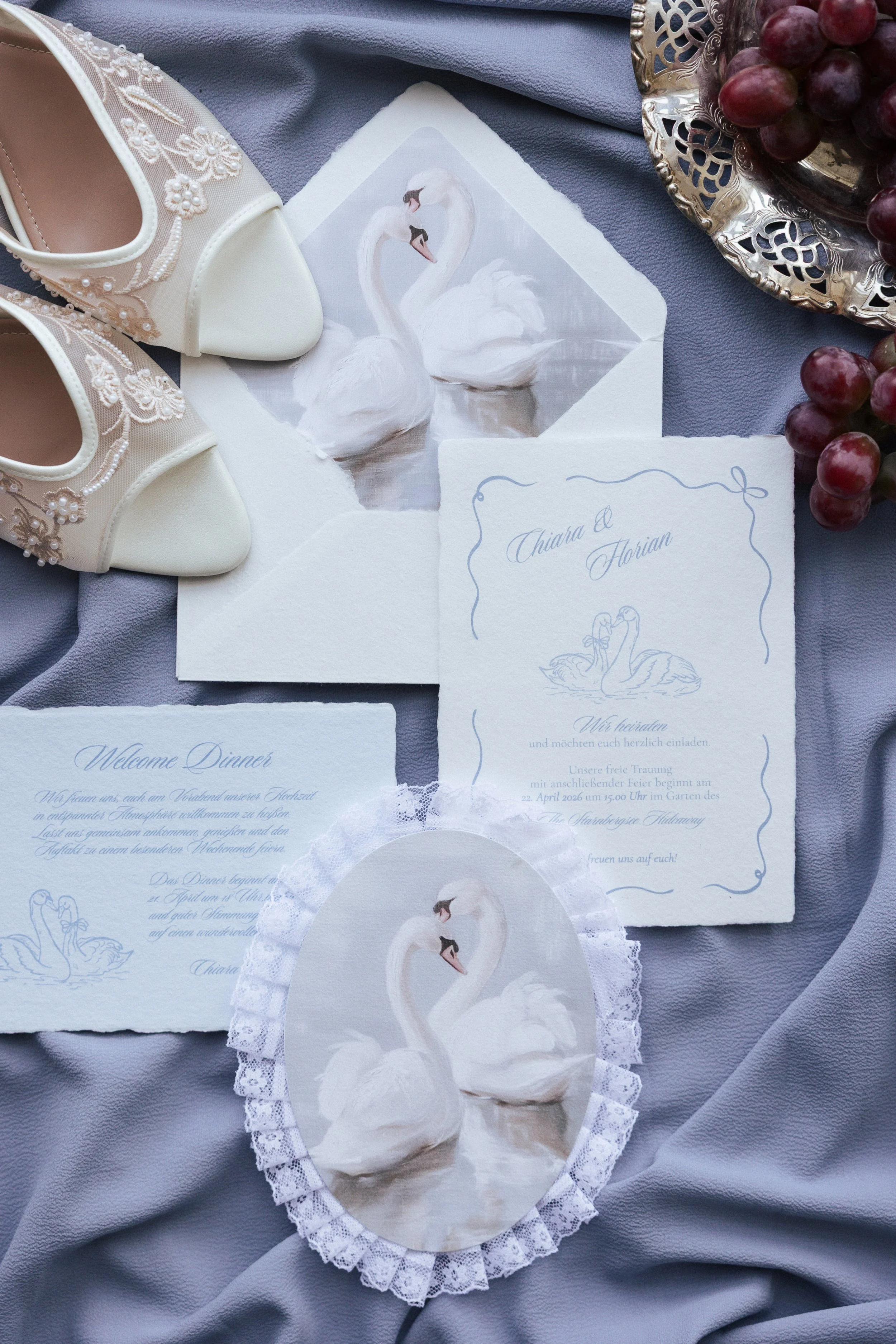 Hochzeitskarten, Schuhe, Traubenschale und Schwäne auf einem grauen Stoff