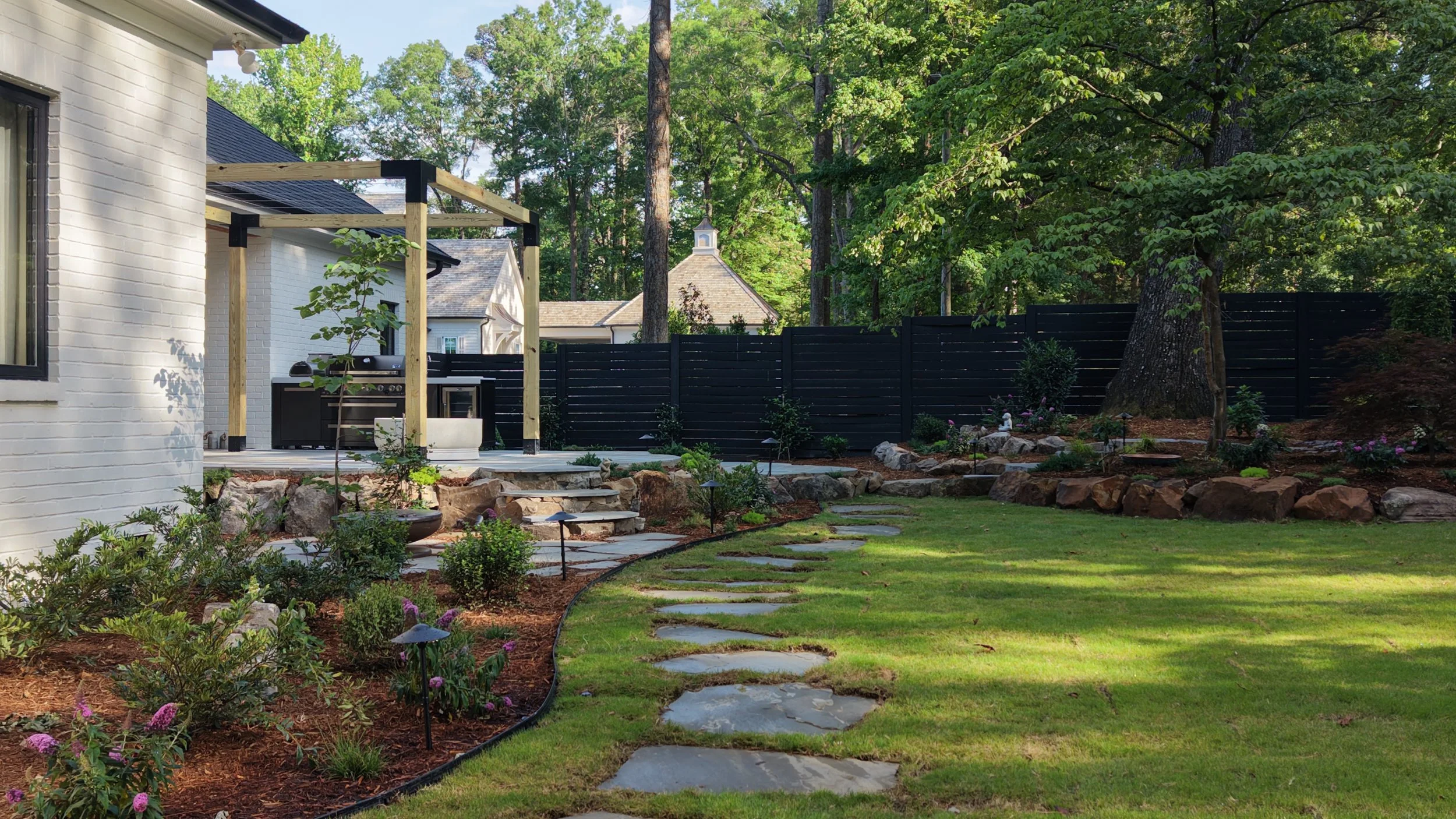 Complete outdoor living space with outdoor kitchen, natural stone, pergola, and landscape lighting in Downtown Cary, NC