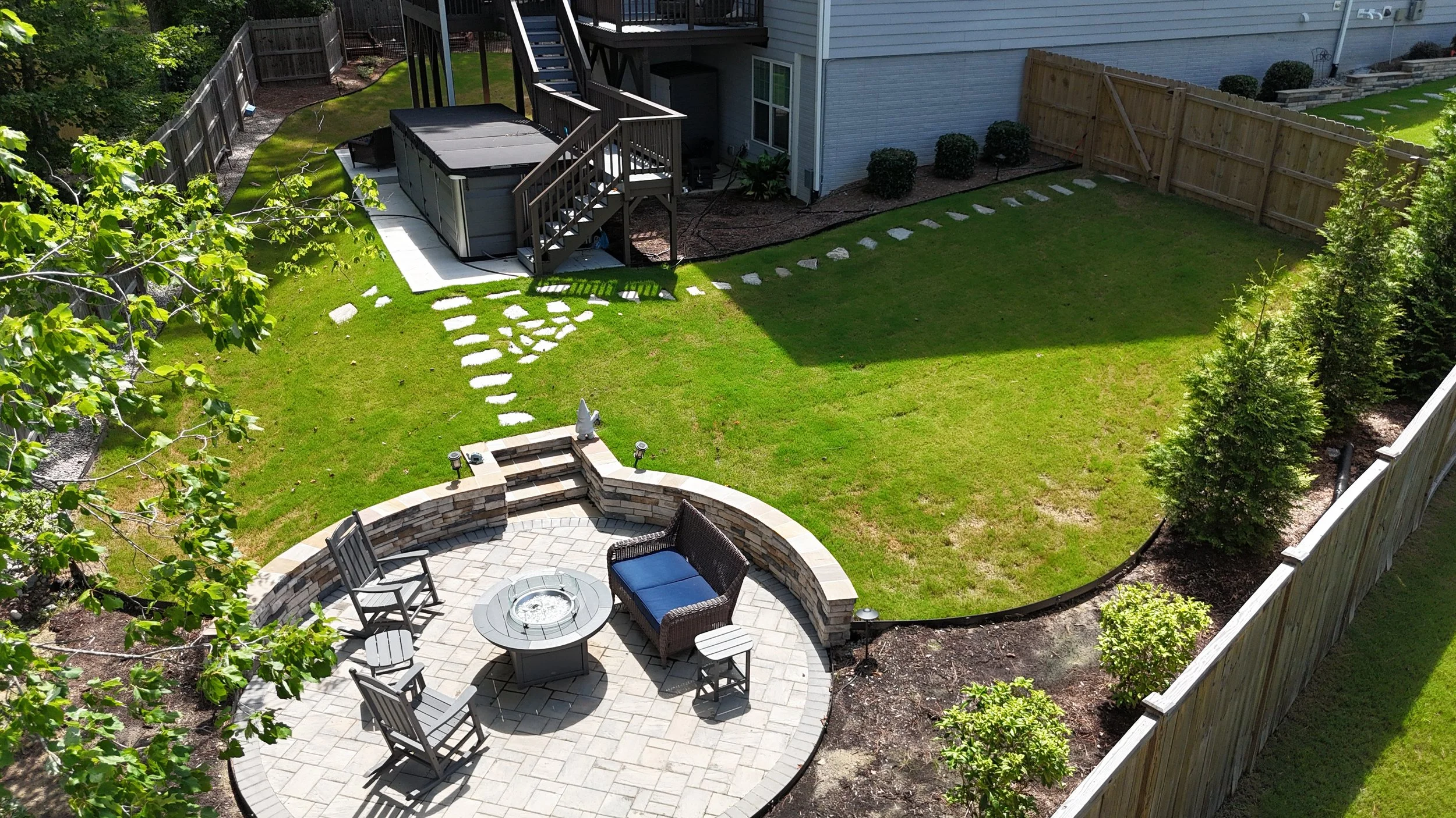 an aerial photo of a backyard with flagstone walkway, fire pit patio and seating retaining wall, lawn, concrete pad with a swim spa, deck, and deck steps in Apex NC preparing for winterization and winter maintenance and care. Wake county NC