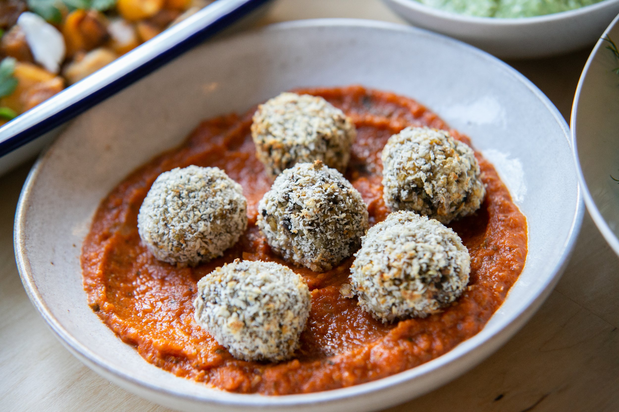 Ball-shaped food rolls coated with oats served on a bed of red tomato sauce in a white ceramic bowl.