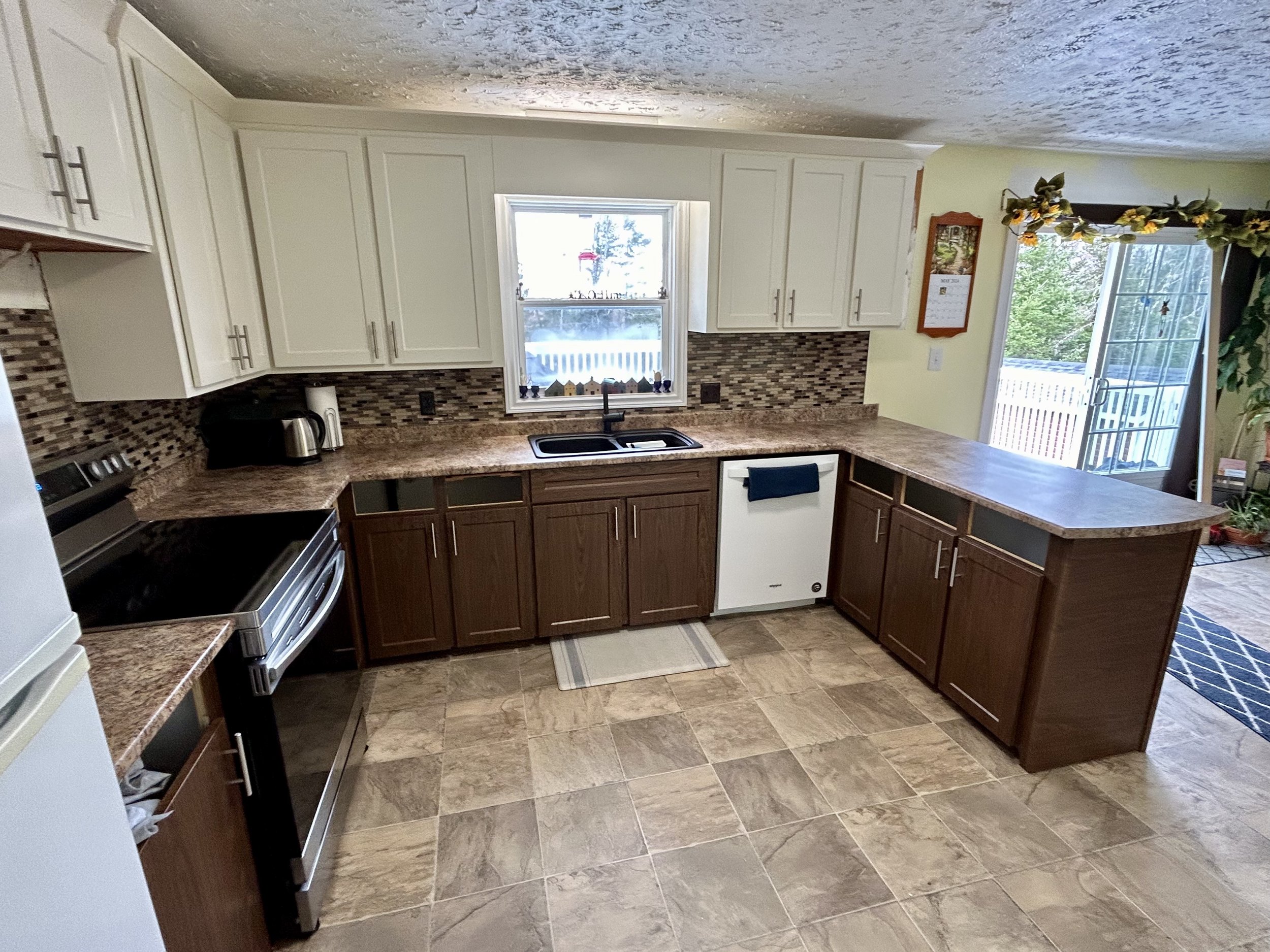 Outdated kitchen with white upper cabinets, brown lower cabinets, granite countertops, with a backsplash of old multicolored tiles.