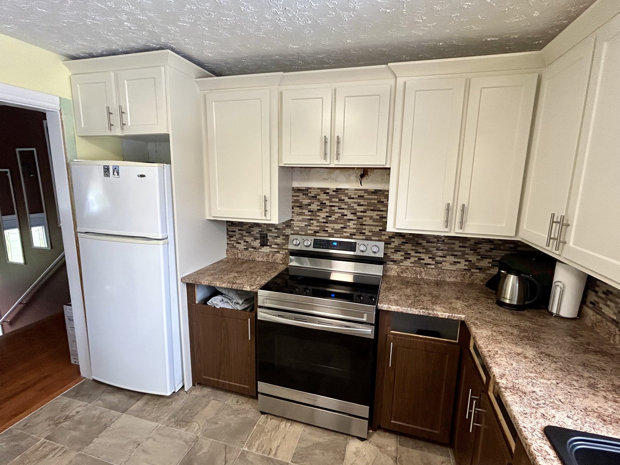 Outdated kitchen with white and brown cabinets, granite countertops, a stainless steel oven, a white refrigerator, and a mosaic tile backsplash.