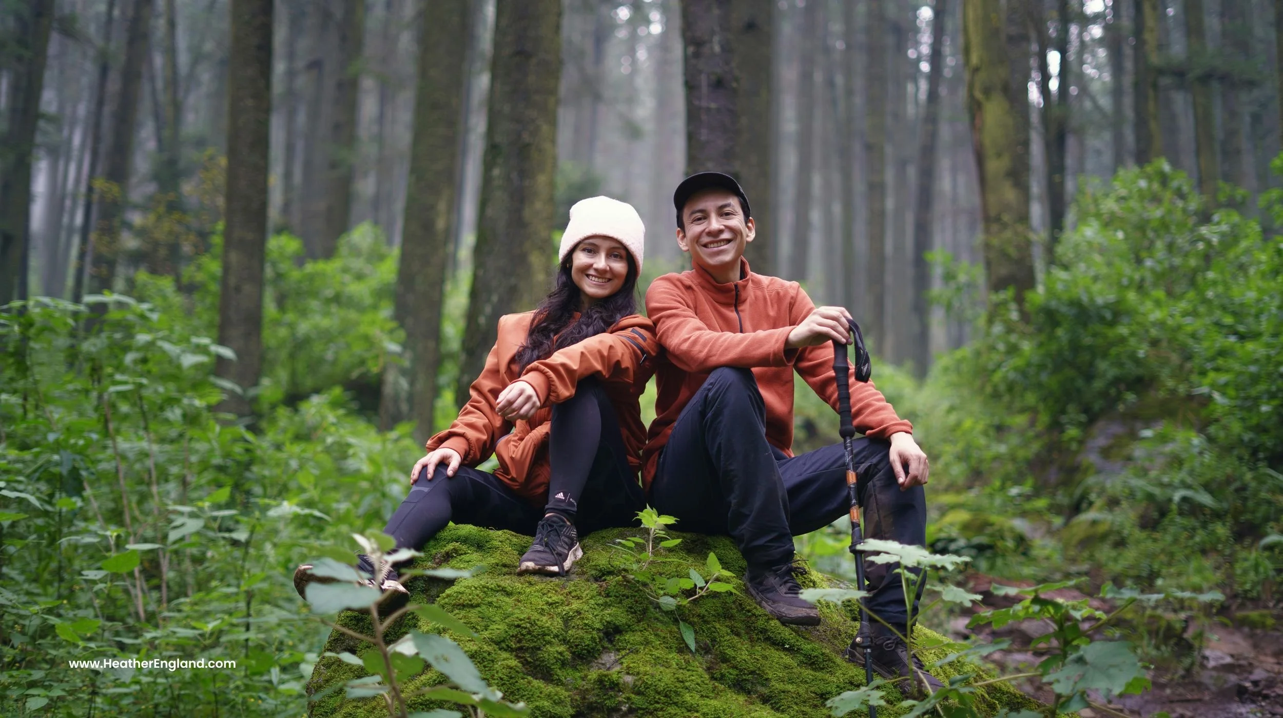 happy midlife couple sitting on mossy rock in the woods out on a hike