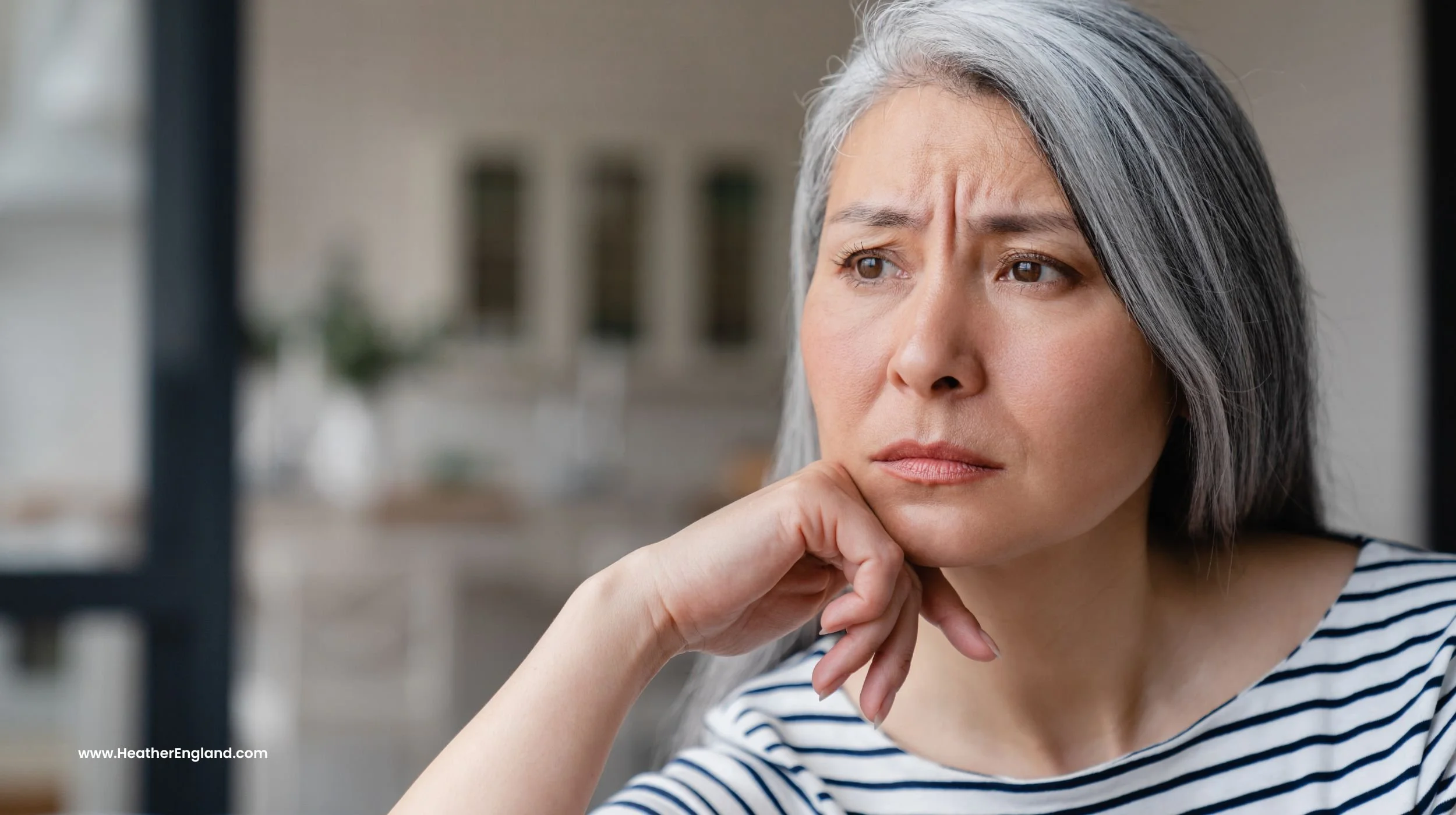 asian midlife woman with grey hair looking sad