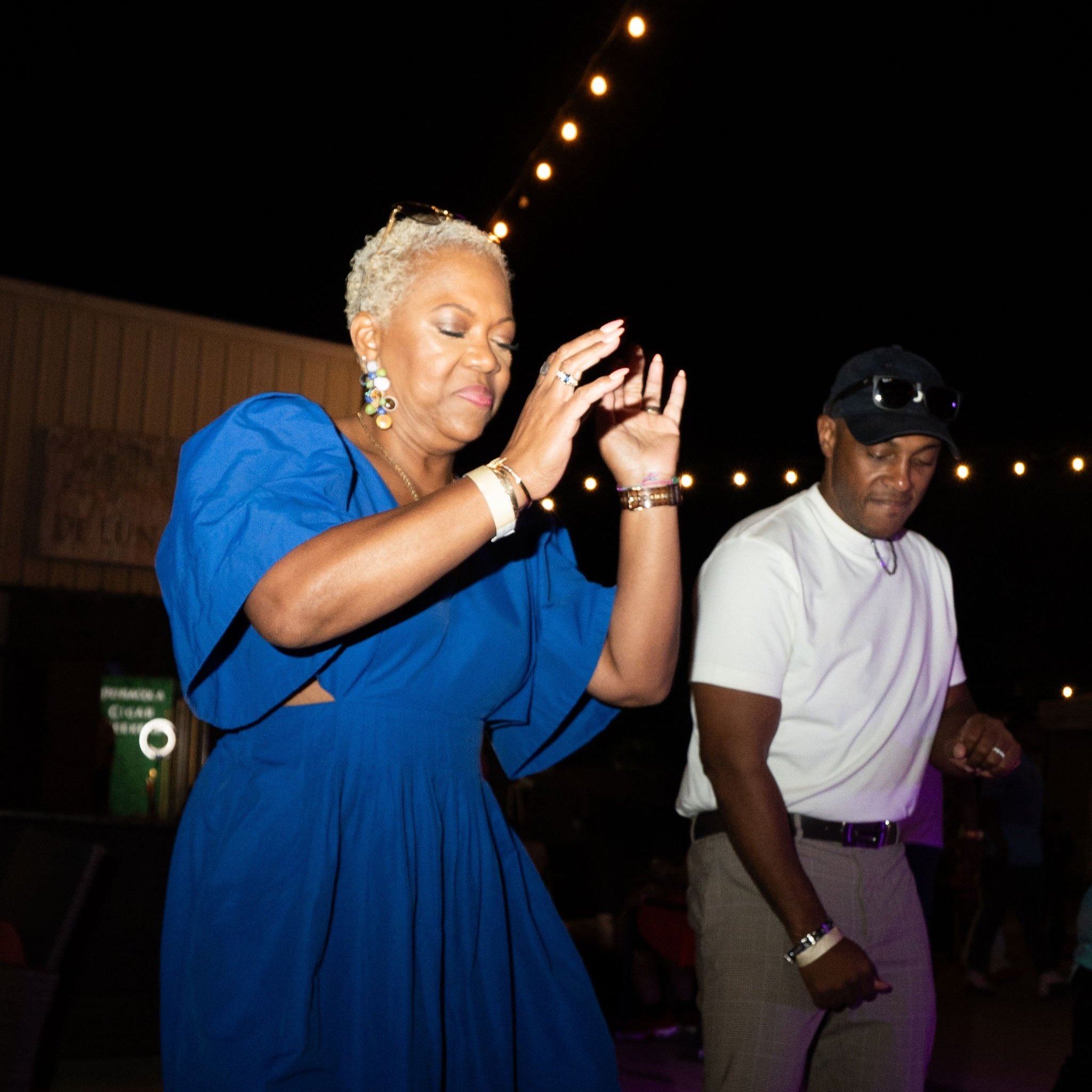 An elderly woman and a middle-aged man dancing at night under string lights.