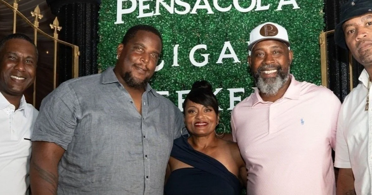 Group of five people smiling at a celebration with a green background that says Pensacola Cigar Tieke.