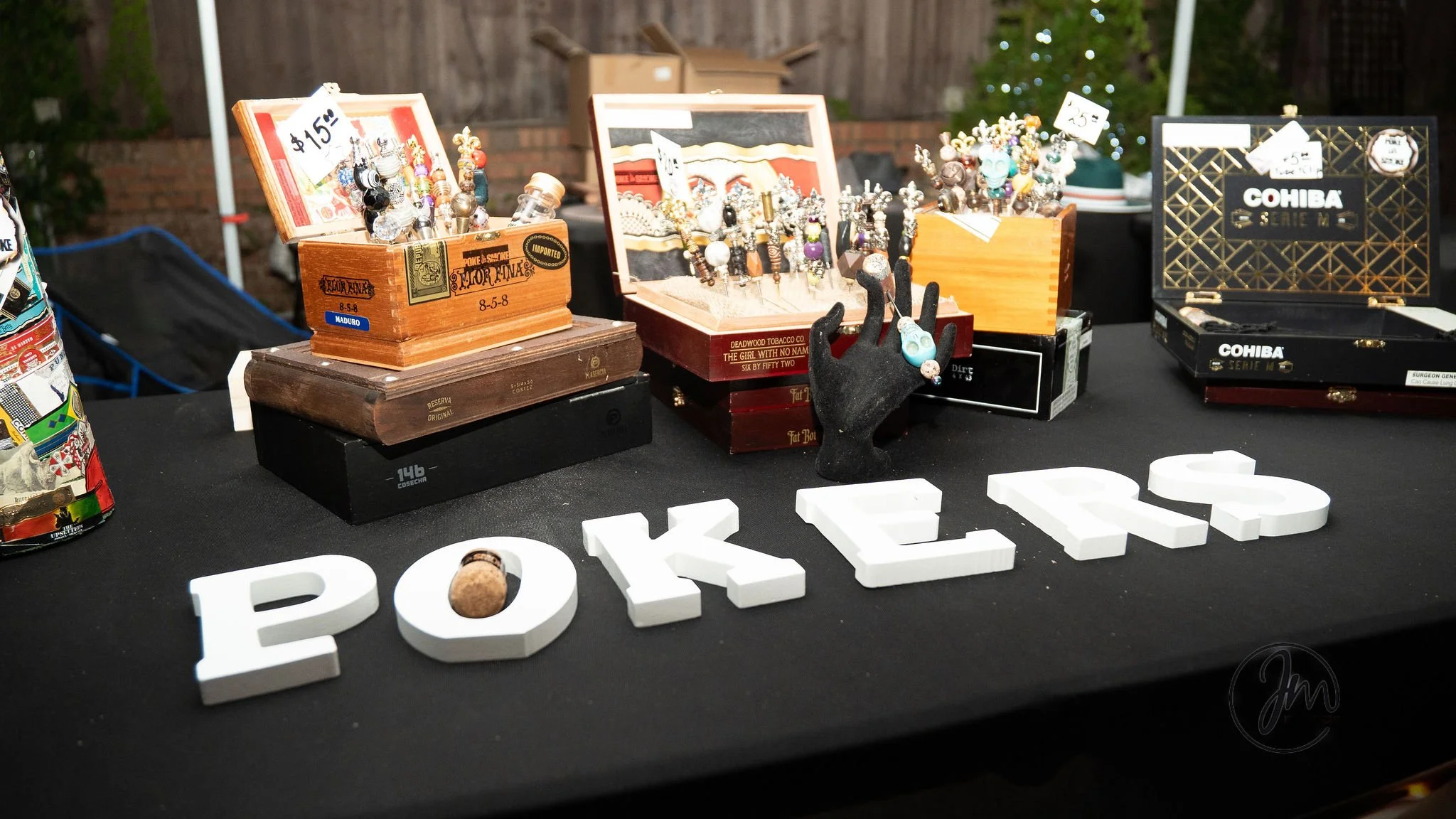 A display table with various jewelry pieces in boxes, including earrings and rings. The table has white block letters spelling 'POKÉMON' on a black cloth. Some jewelry is displayed with price tags, and there's a decorative black hand mannequin holdin