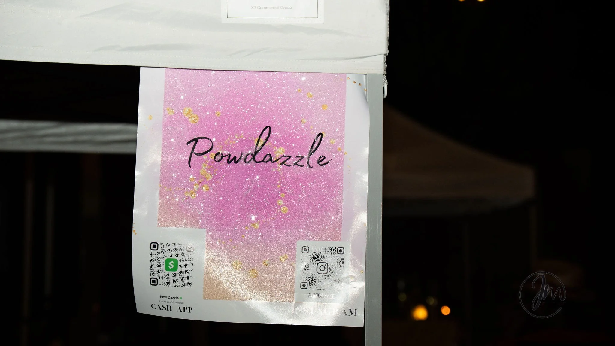 Pink and gold sparkly sign with the word 'Powdazzle' in cursive font, attached to a metal pole at night.