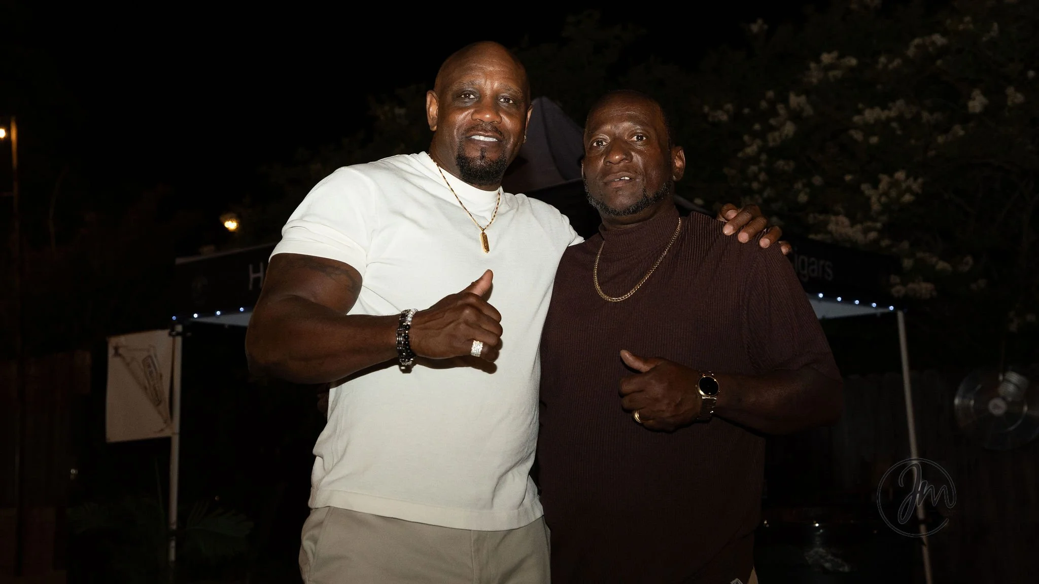 Two men standing close together at night, smiling and posing for the camera, with their arms around each other.