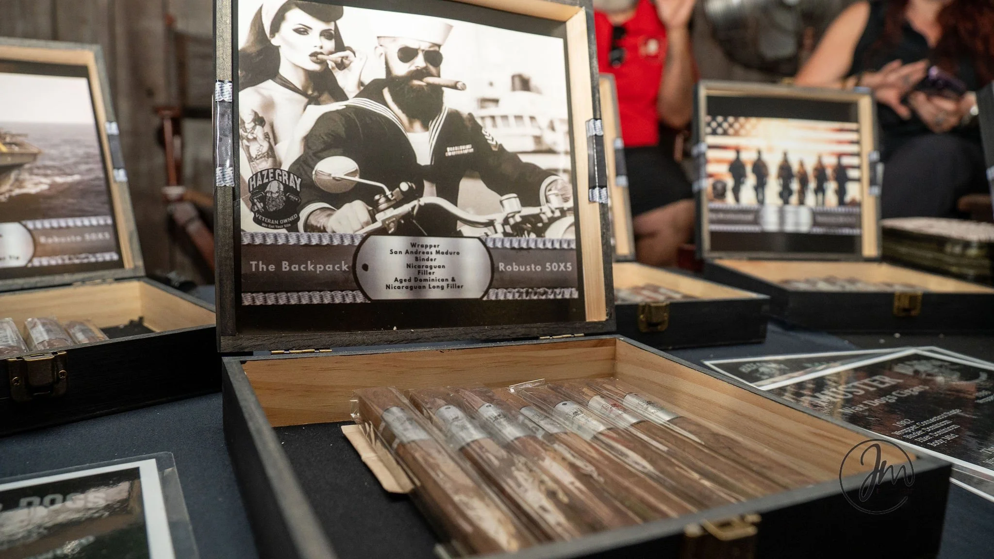 Open display box containing cigars with a picture of a man and woman on the inside of the lid. The man has a beard and is riding a motorcycle, while the woman has dark hair and is smoking a cigar. There is a sign with text describing the cigars insid