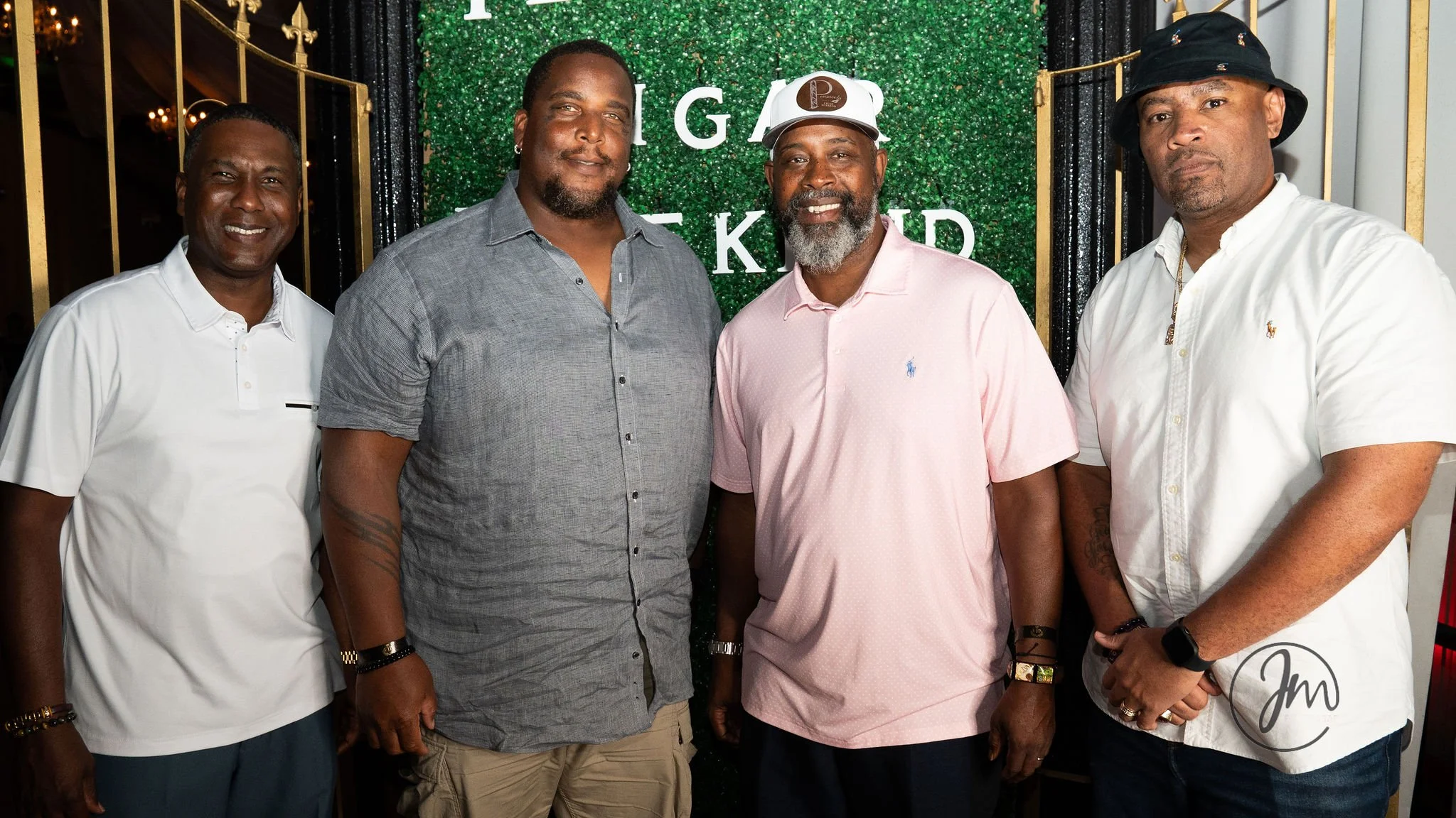 Four men standing side by side at an indoor event with a green background with white text and decor.