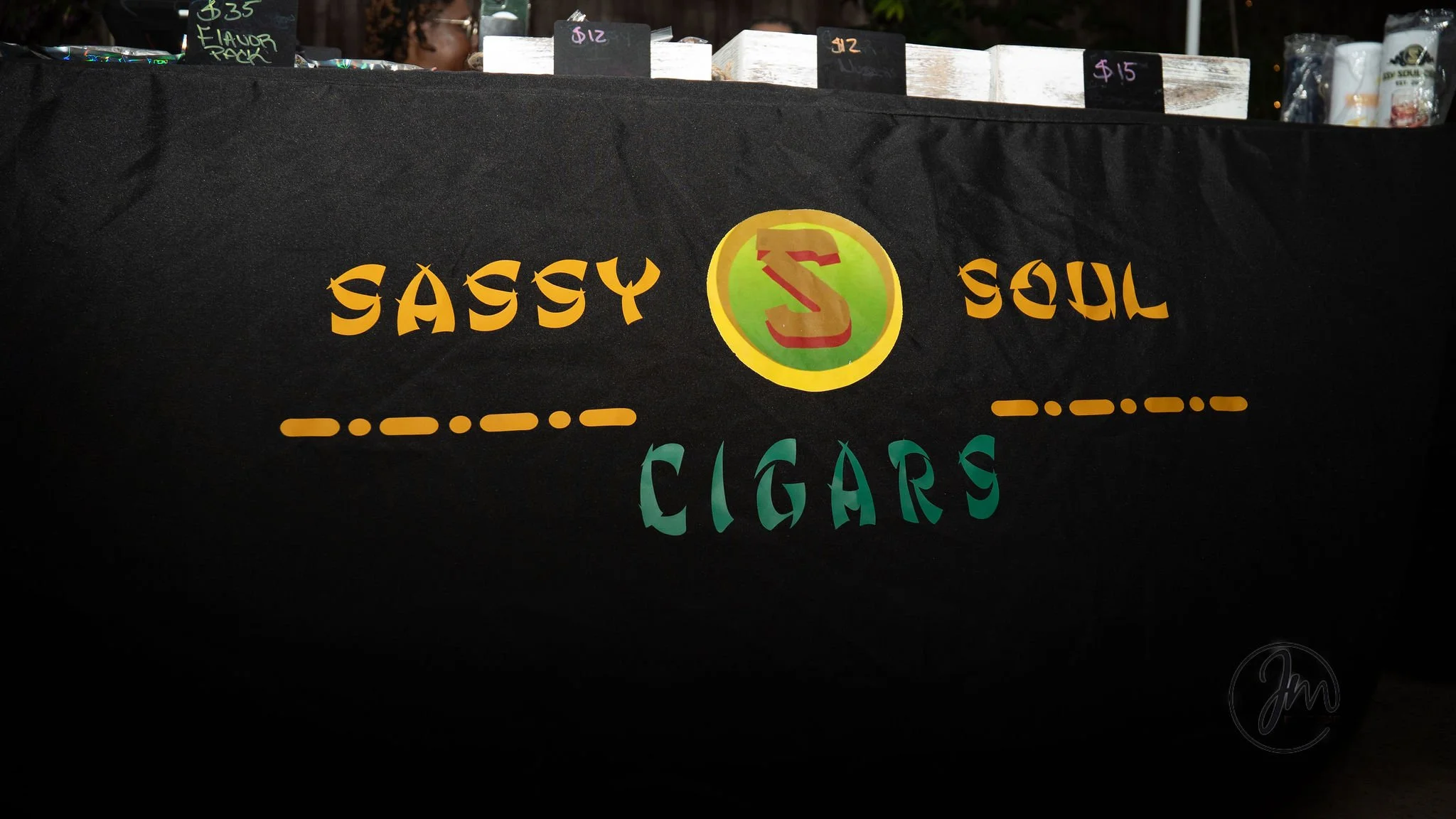 Sign for Sassy Soul Cigars featuring colorful lettering and logo on a black background.
