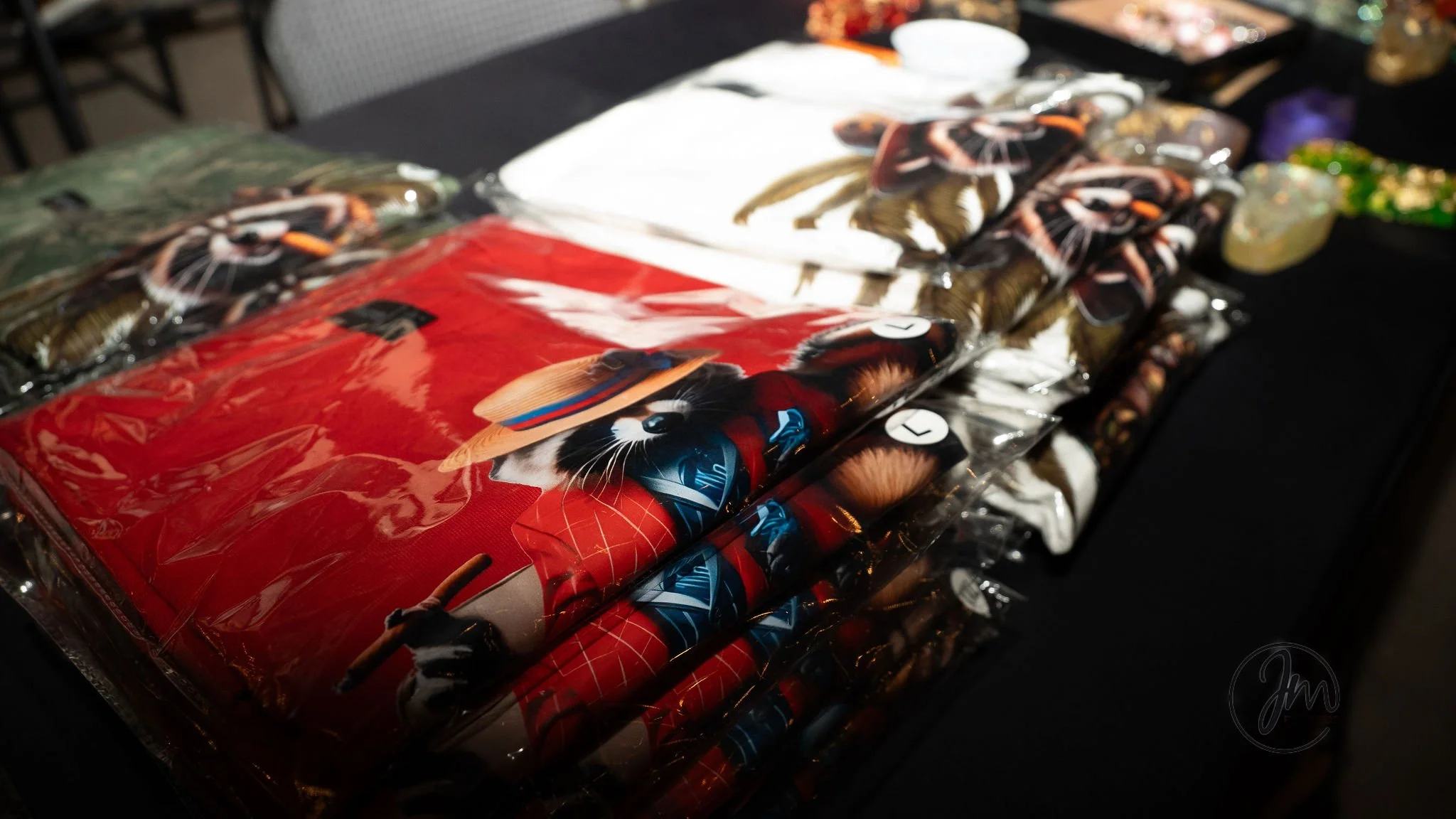 Clear plastic bags containing various cat-themed clothing and accessories are laid out on a black table, with some white, green, and purple items visible in the background.