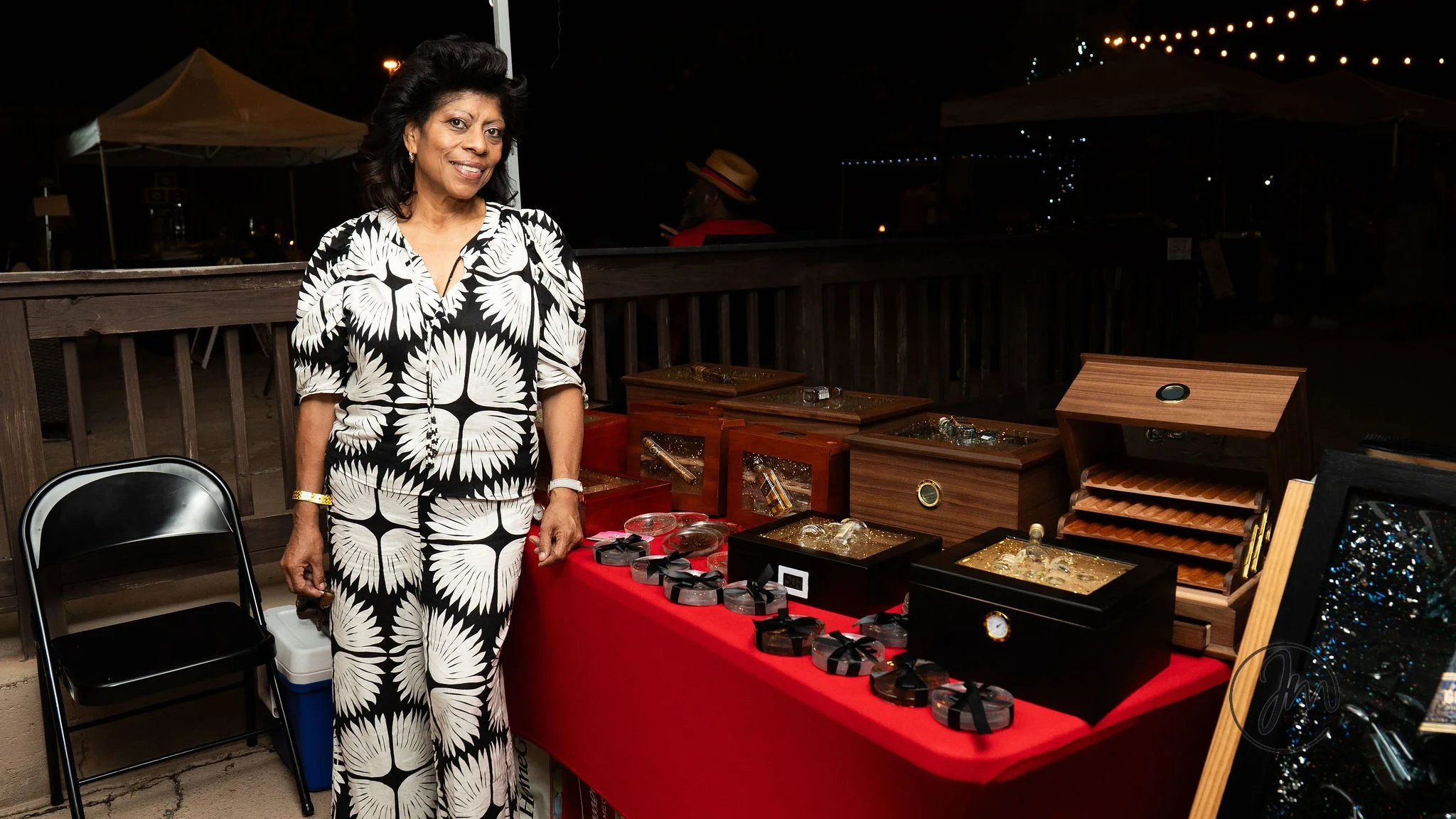 Woman standing next to a display table of jewelry and watch boxes at an outdoor market at night.