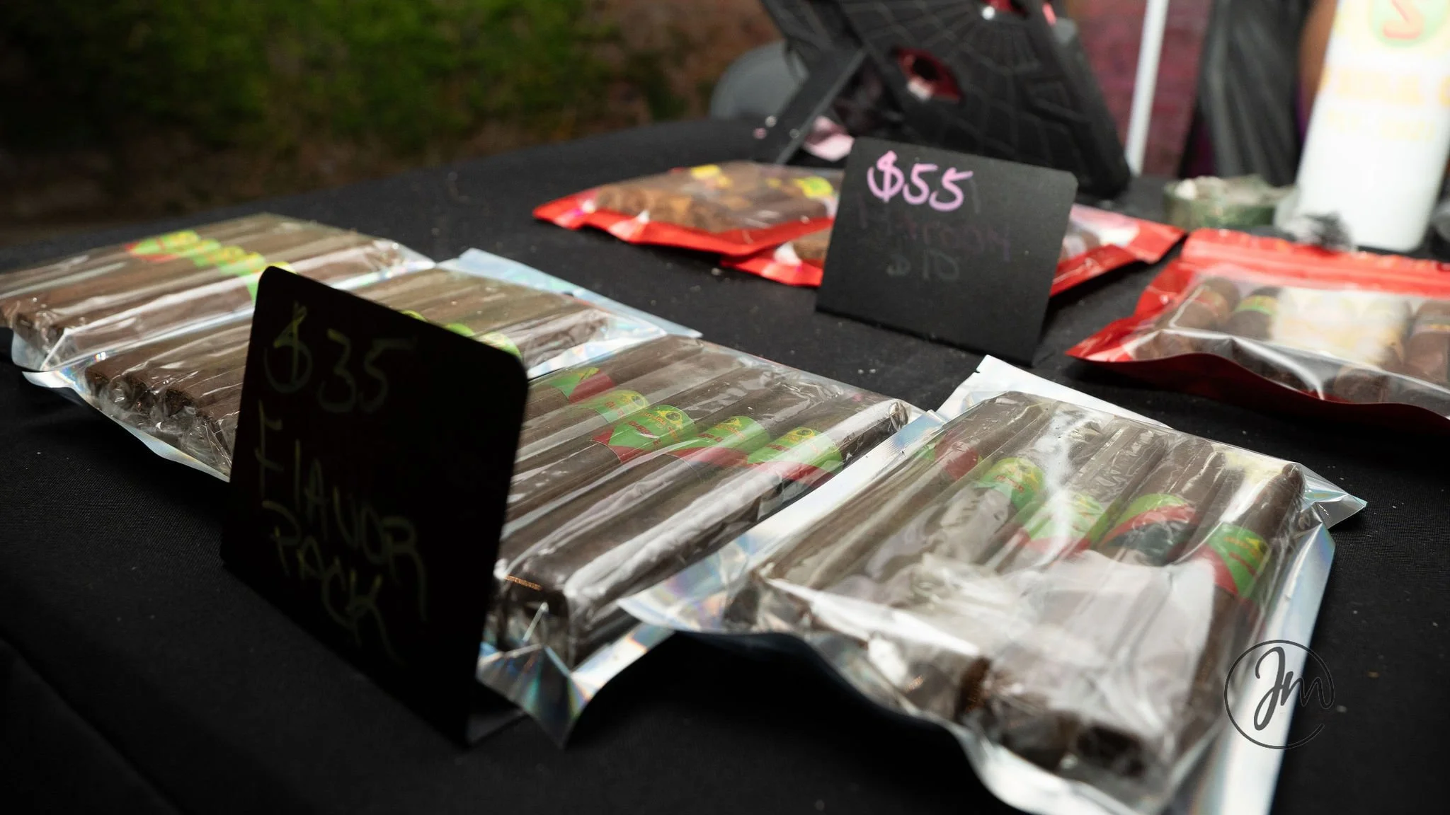 Chocolate cigars wrapped in clear plastic with painted green and red labels, priced at $35, on a black table at an outdoor night market.