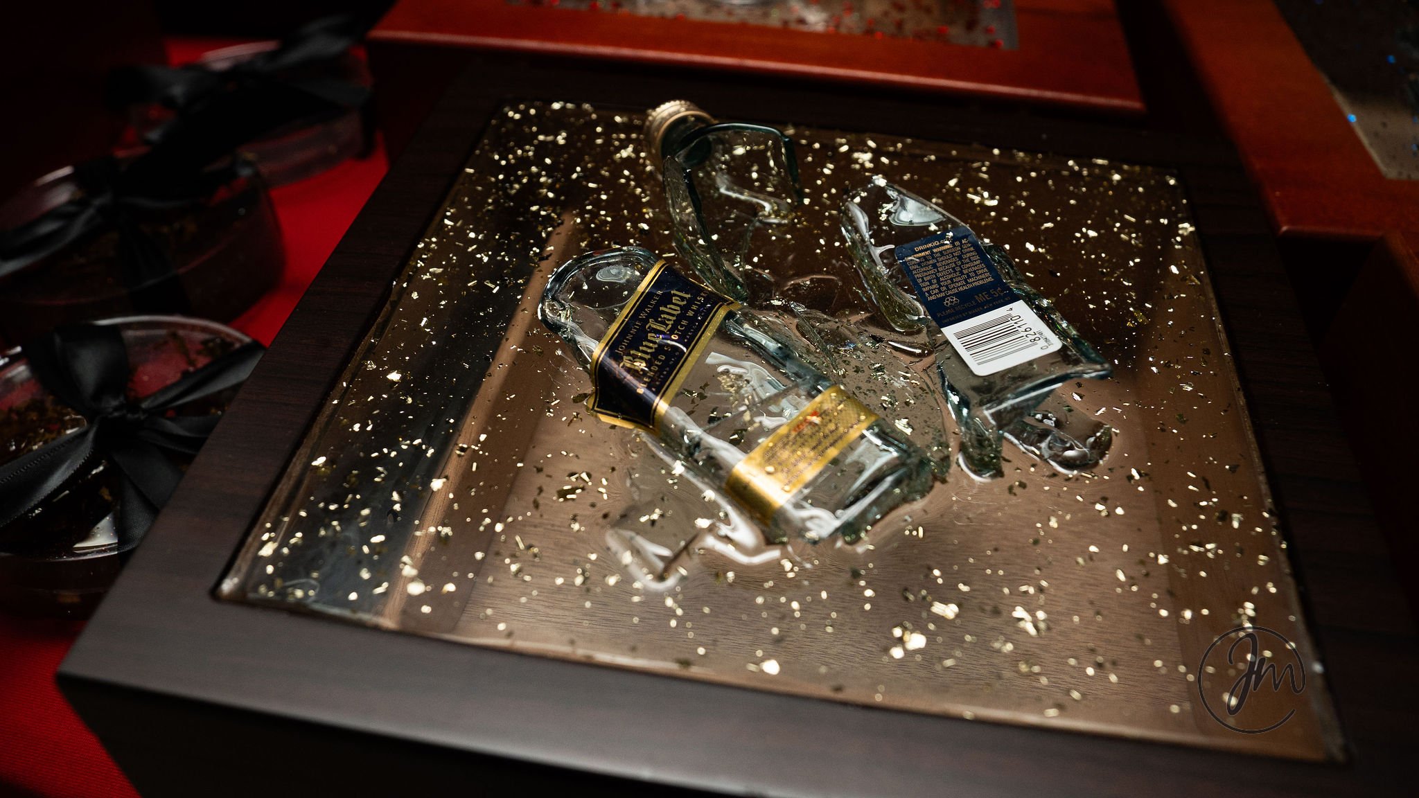 Broken glass bottles and shards on a mirrored surface with gold specks, on a wooden table.