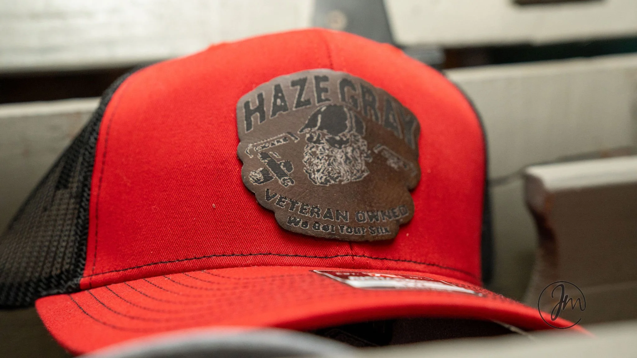 A red and black baseball cap with a patch on the front that reads "Hazegard Veteran Owned" and features an image of a bearded man wearing a helmet.