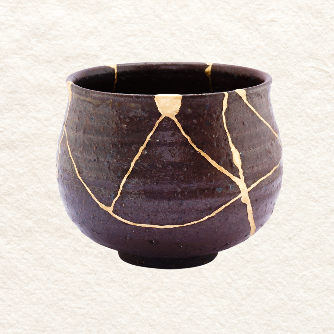 A dark brown ceramic Japanes kintsugi bowl with gold decorative lines on its surface.