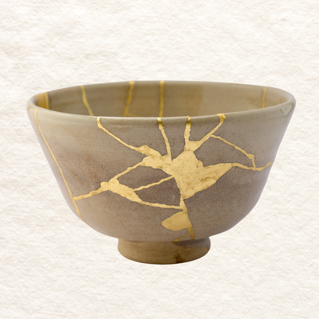 A ceramic kintsugi bowl with a beige and gray glazed finish, decorated with gold-colored crackle lines.