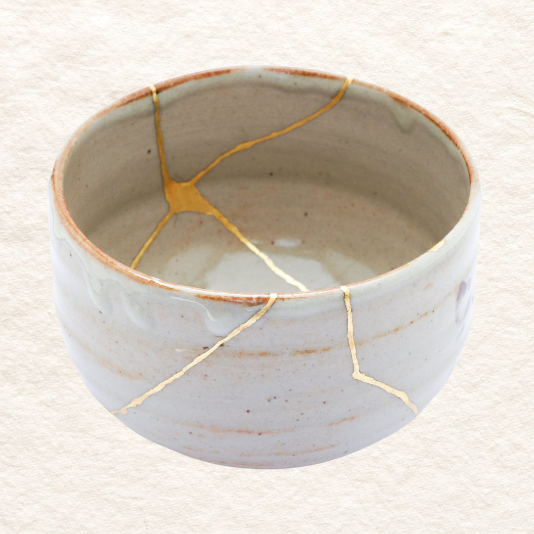 A white ceramic bowl with visible cracks repaired with gold, known as kintsugi.