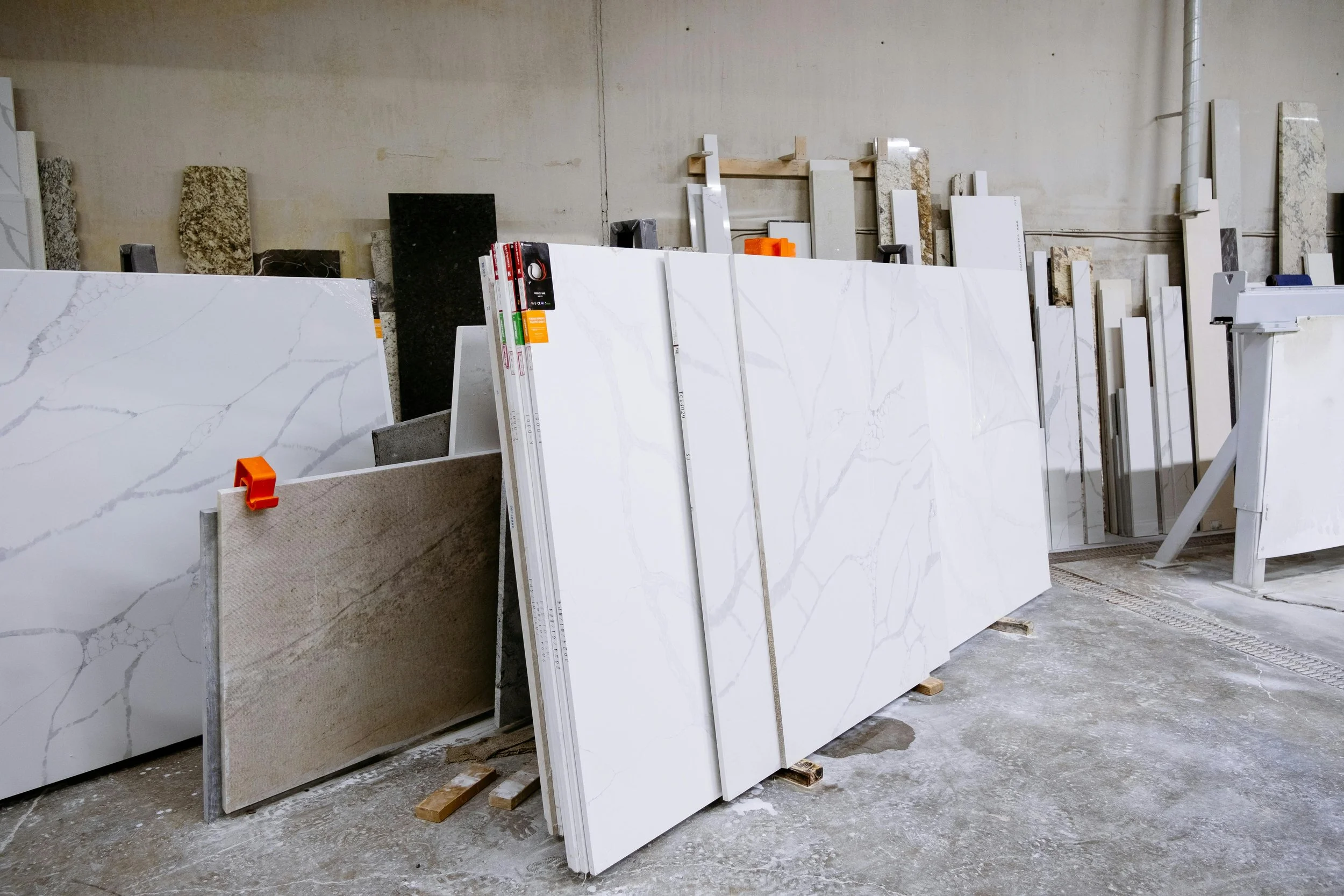 Large slabs of marble and quartz in a warehouse, leaning against a wall and supported by wooden pallets, with various patterns and colors.