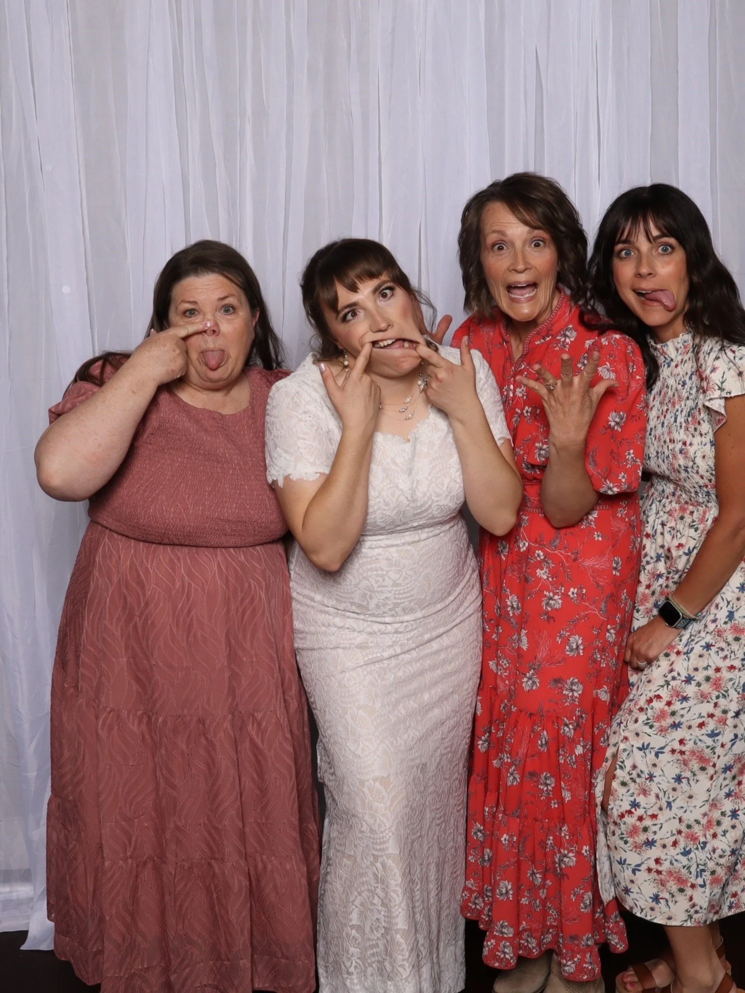 Four women standing together against a white backdrop, making funny faces, sticking out their tongues, and posing playfully.
