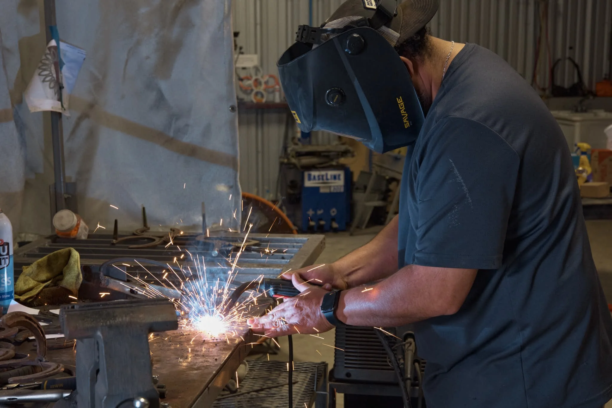 A person welding metal in a workshop, wearing a protective welding helmet and gloves, sparks flying from the welding process.