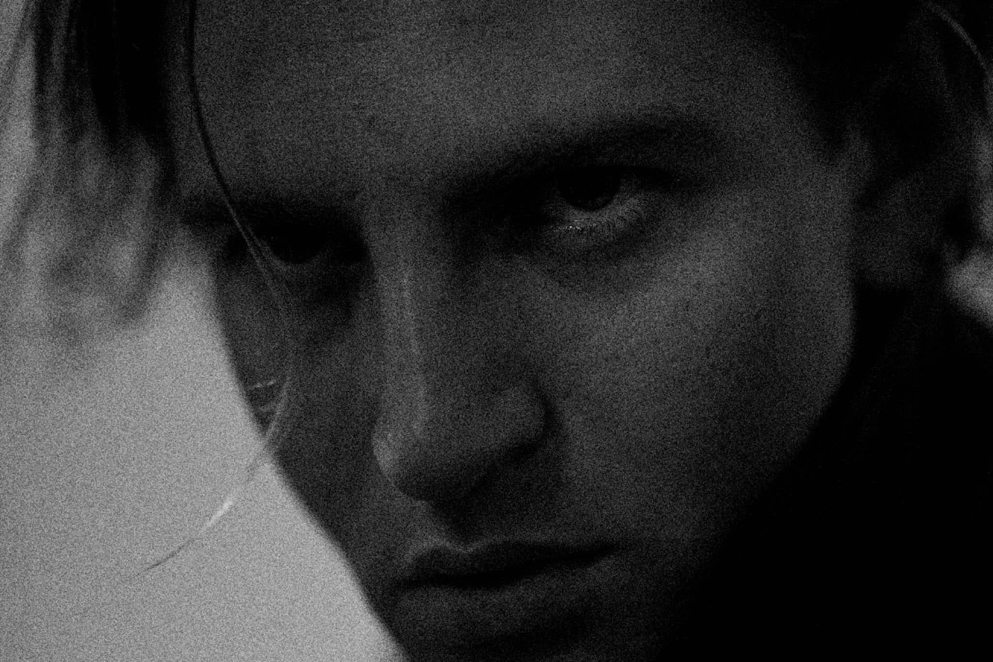 Close-up black and white portrait of a woman with a serious expression, looking directly at the camera.