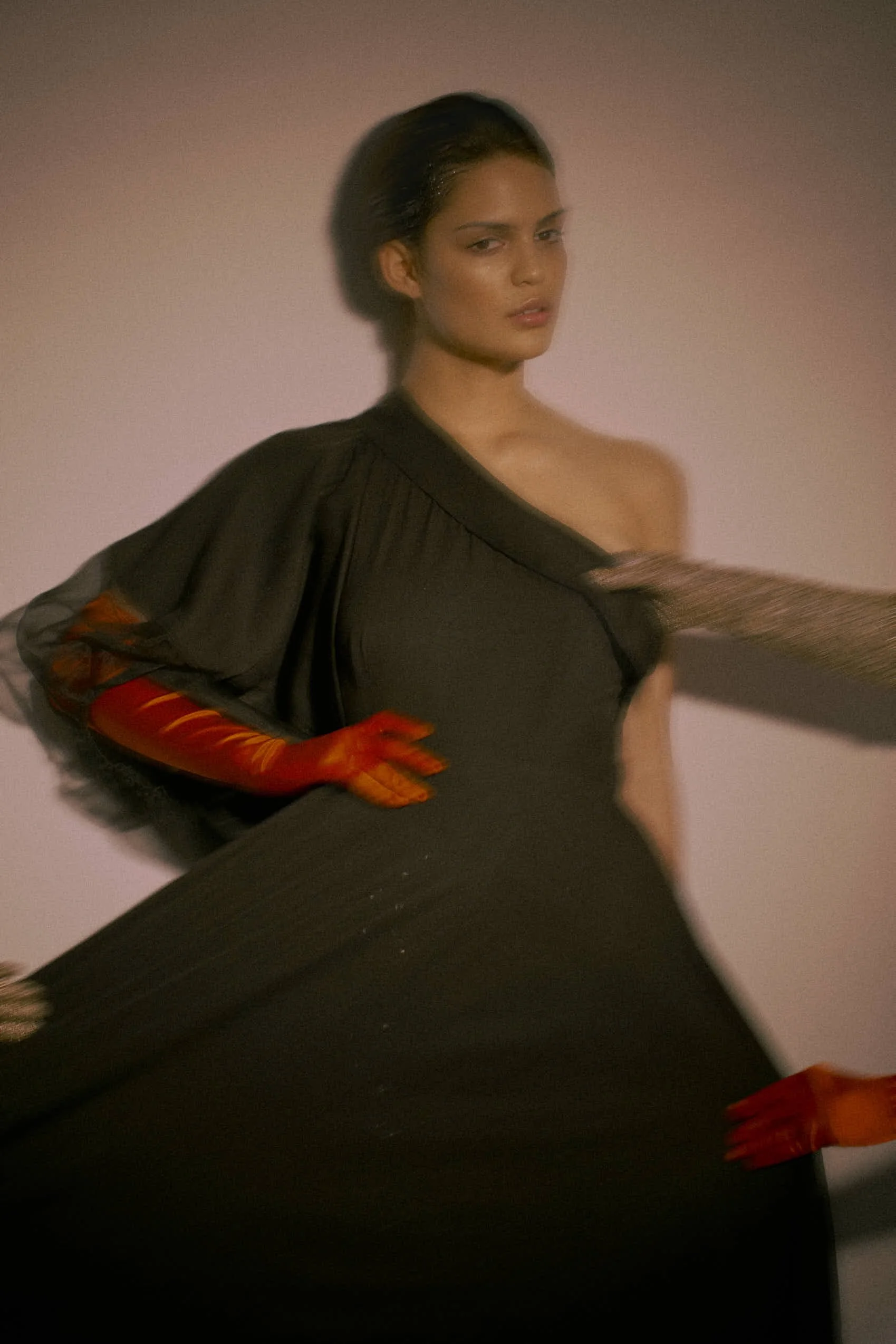 Fashion model posing in a black one-shoulder dress with long gloves, standing against a plain background.