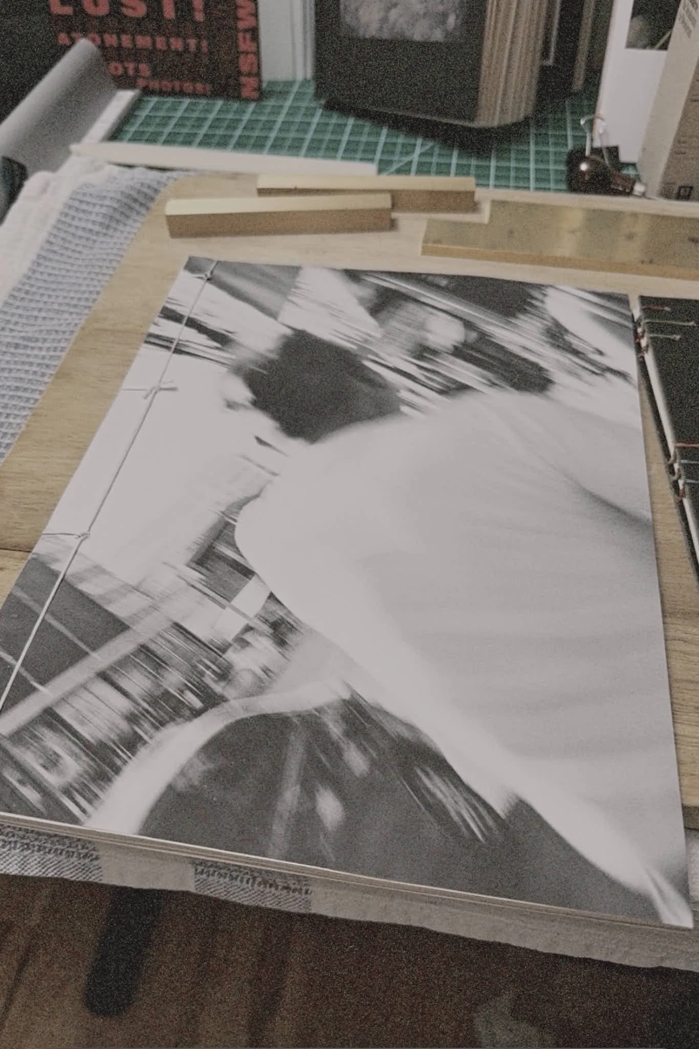 Black and white photograph of a person walking on a city street, with objects and buildings in the background.
