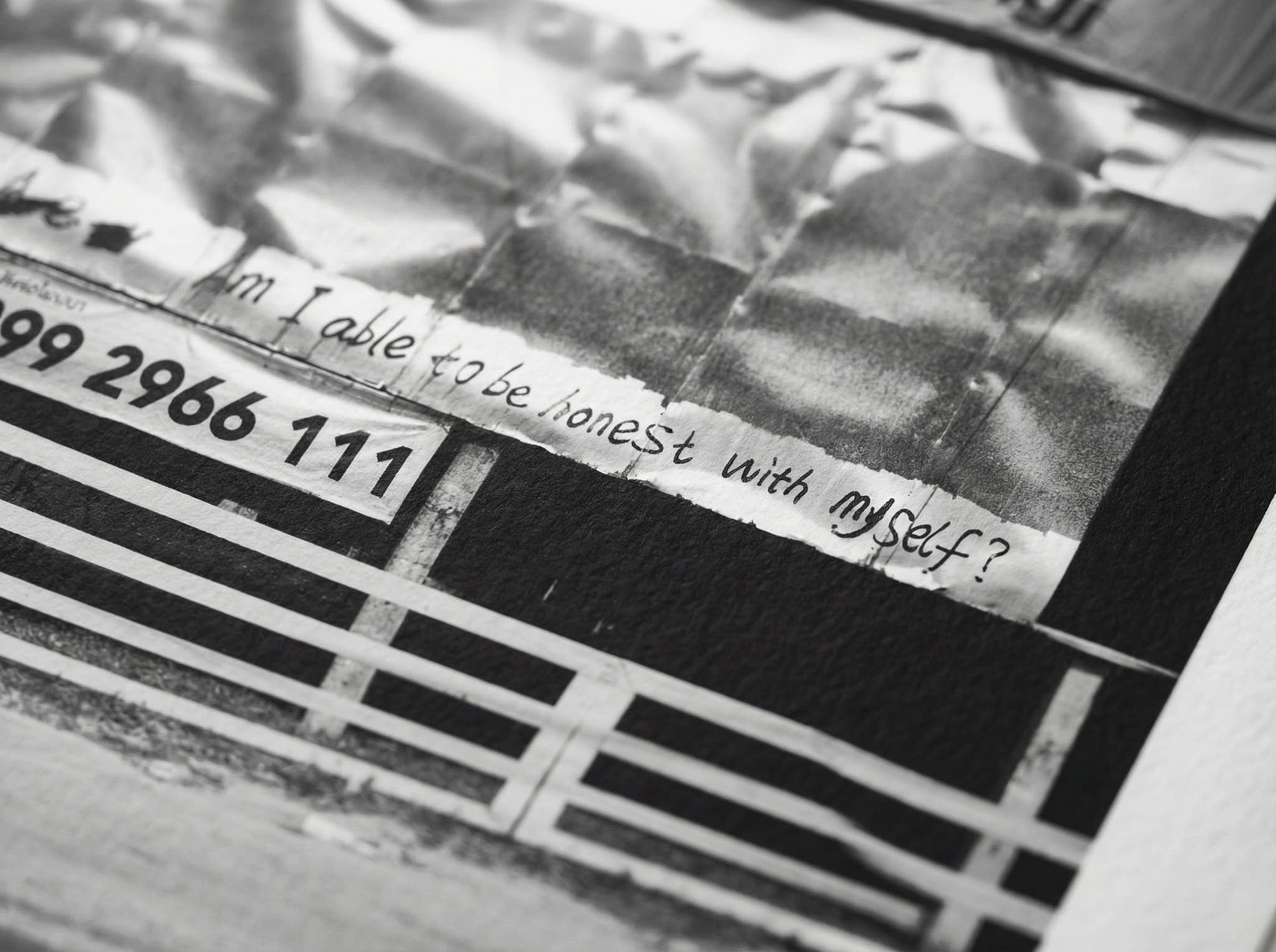 A black-and-white newspaper clipping featuring a handwritten message that says, 'Am I able to be honest with myself?' and a partially visible phone number '299 266 111' below it.