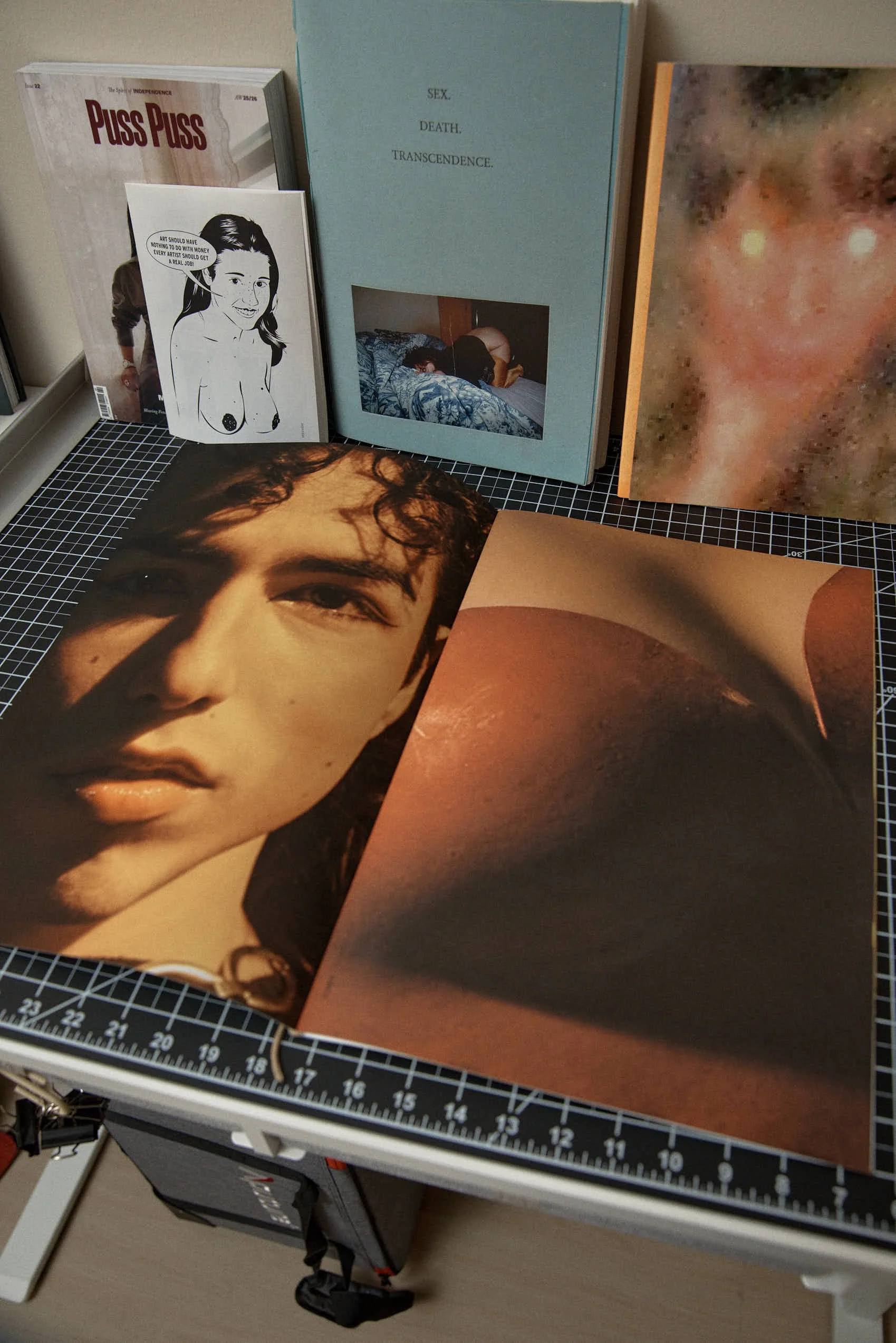 A collection of art books, photographs, and prints displayed on a grid cutting mat surface, featuring portraits, abstract art, and book covers.