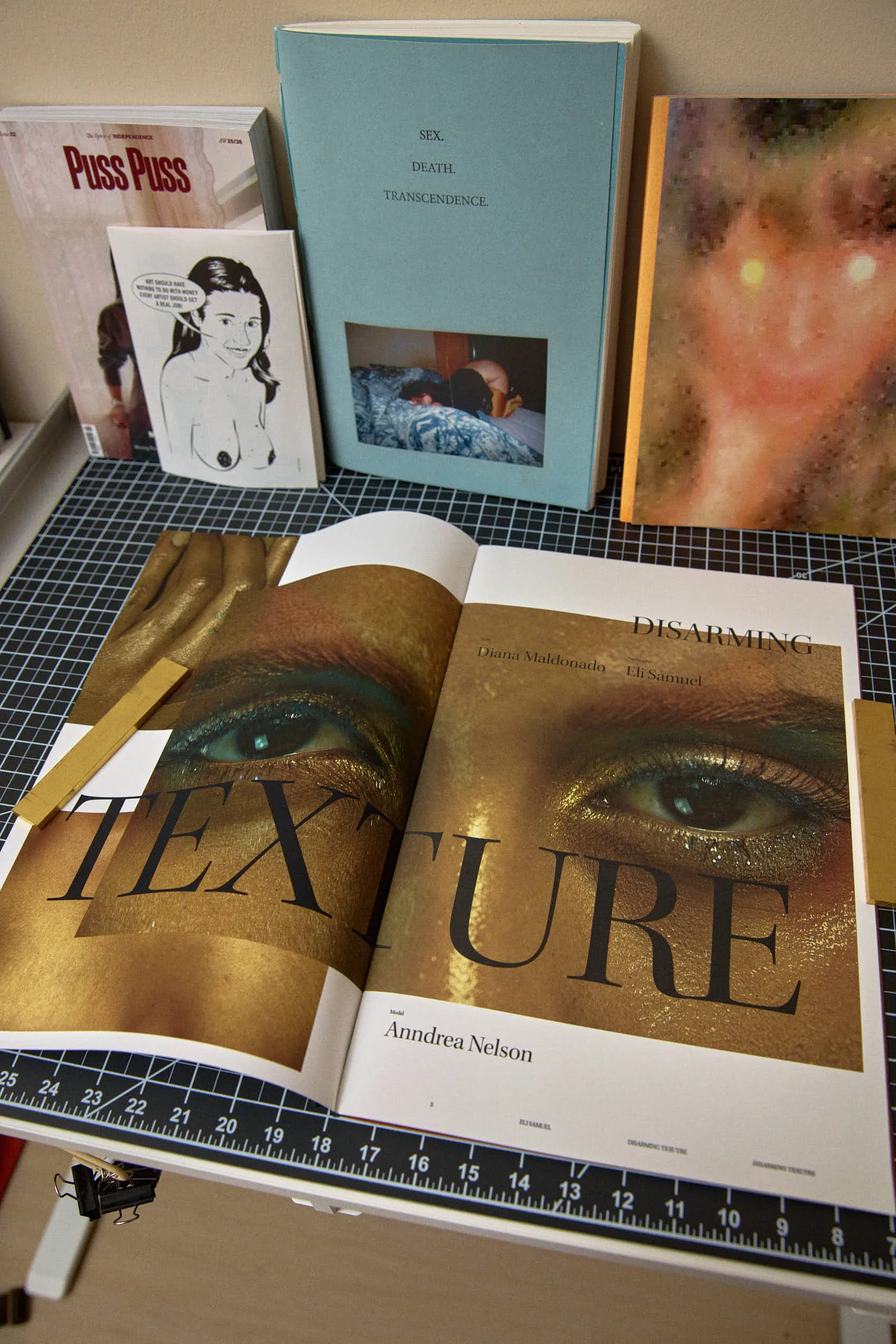 Open magazine displaying a large photo of a person's eye with gold makeup, with the words 'TEXTURE' and 'DISARMING' and authors' names.