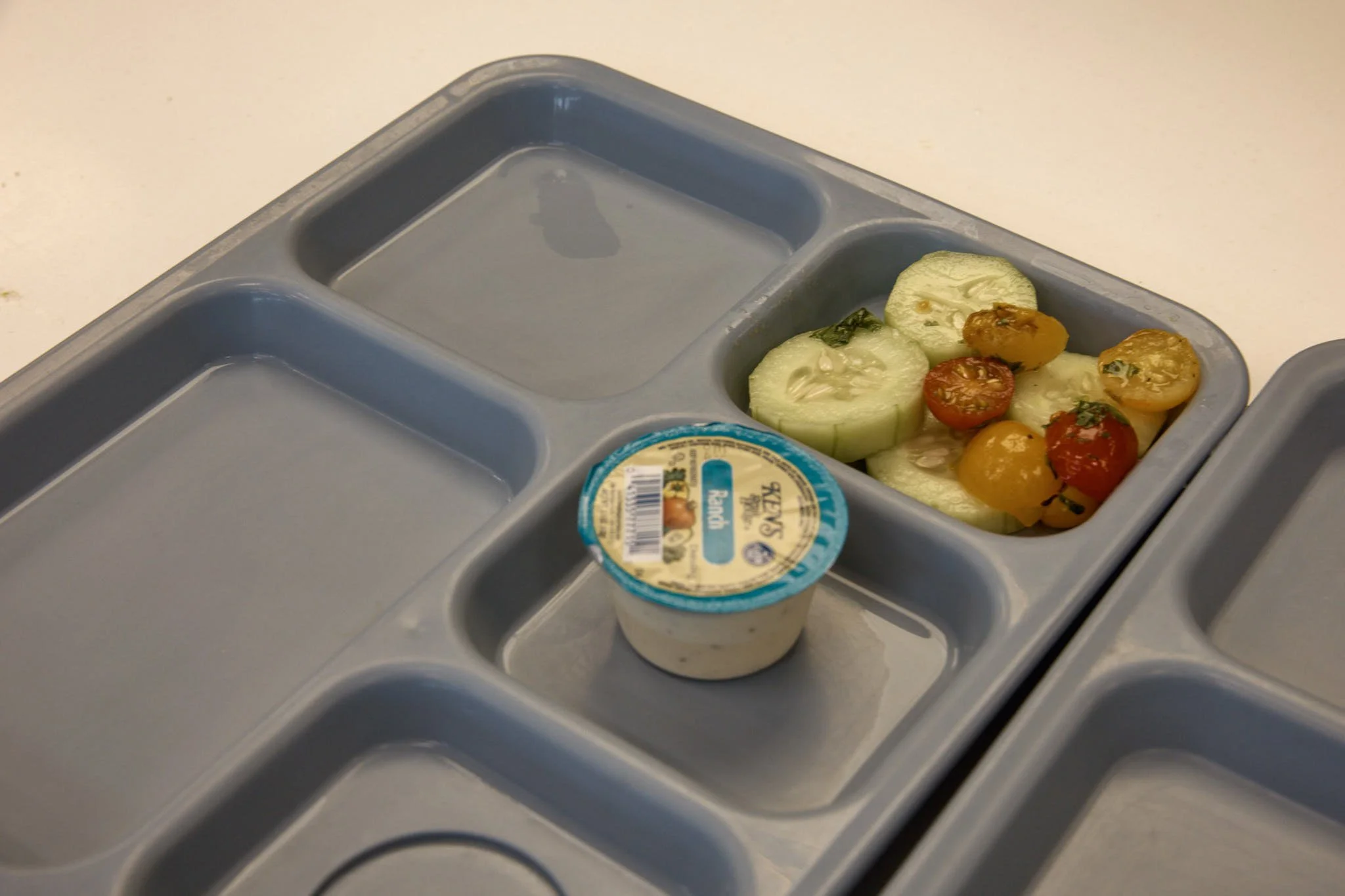 School lunch tray with sliced cucumbers, cherry tomatoes, and a small container of Ranch dressing.