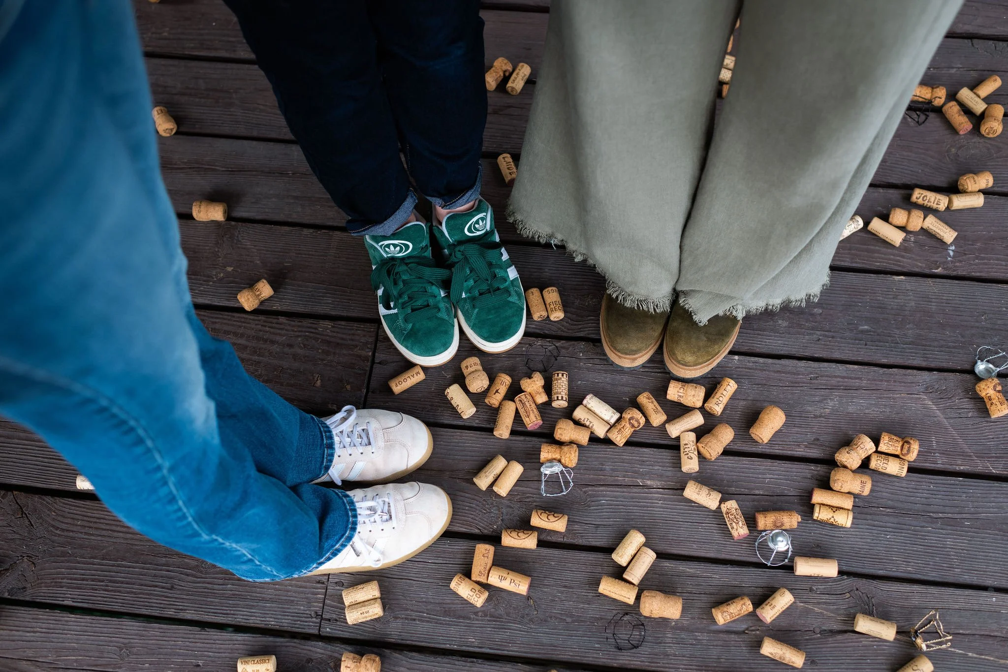 People standing in a circle on a wooden deck, surrounded by scattered corks and small string lights, taken from above.