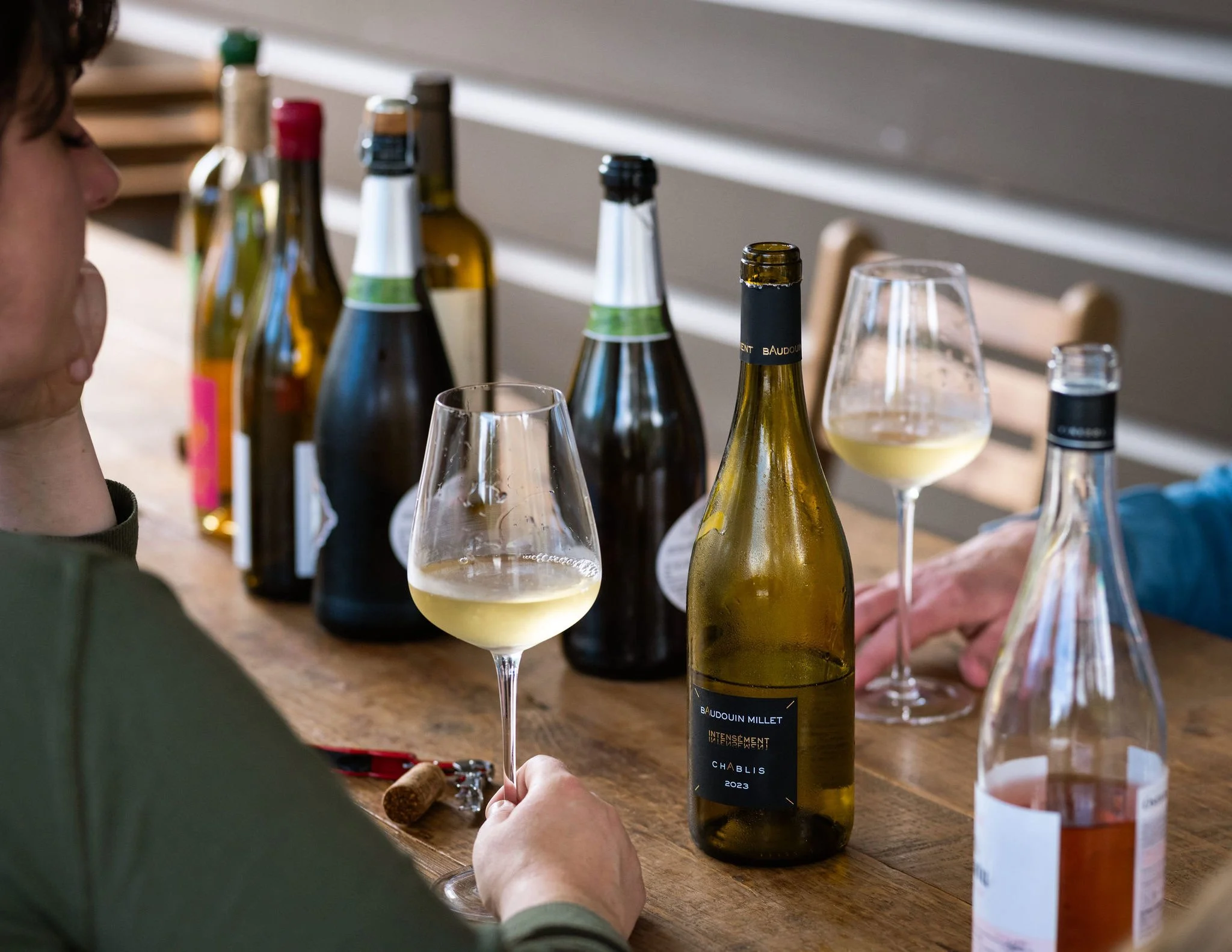 People sampling white wine with several bottles of wine on a wooden table.