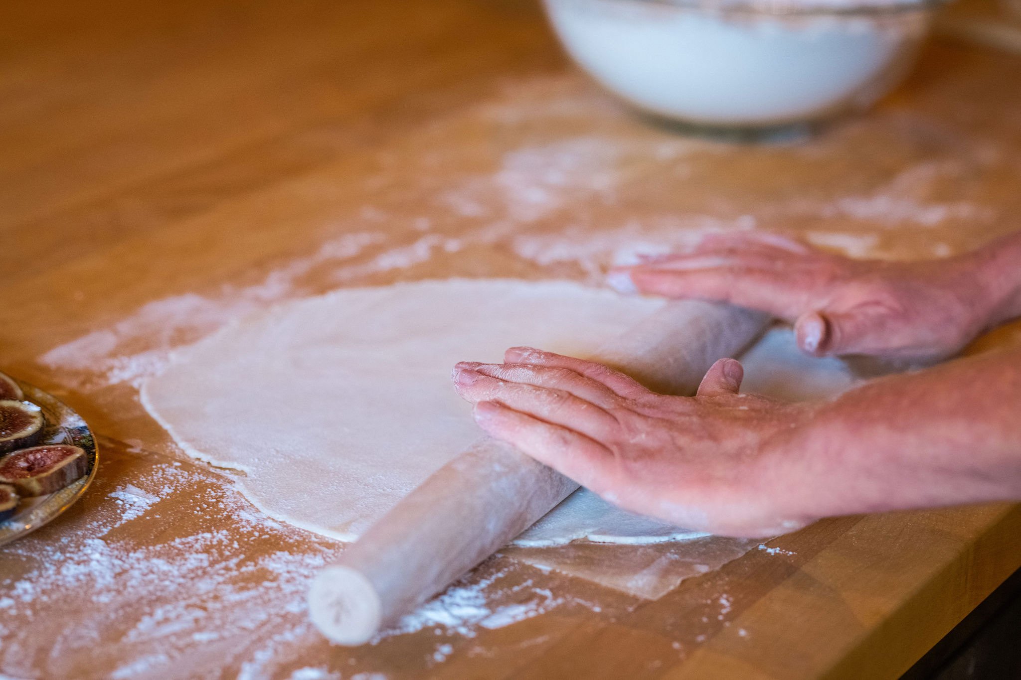 Hands rolling out dough on a floured wooden surface for baking.