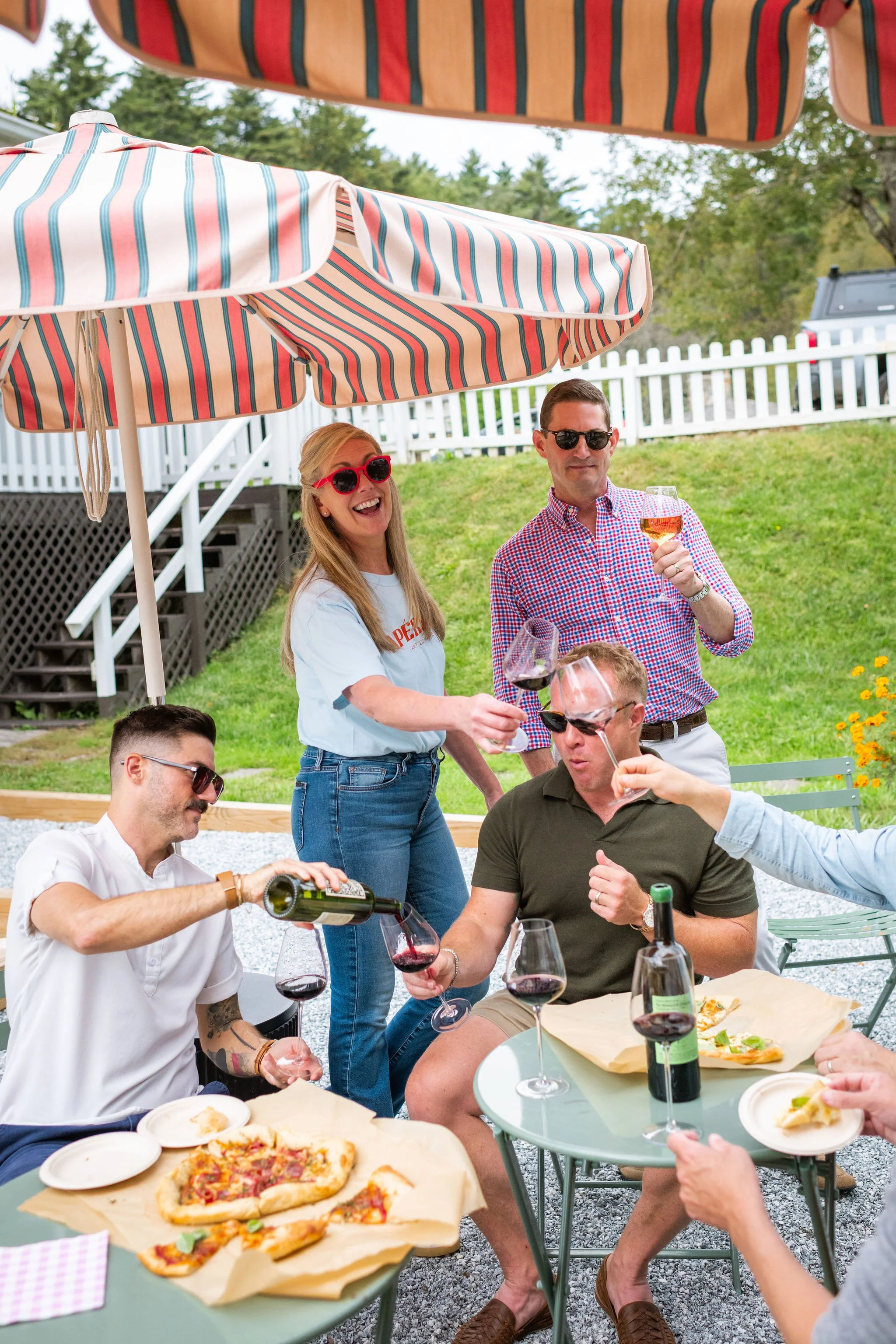 People enjoying a backyard outdoor party with wine, pizza, and umbrellas.