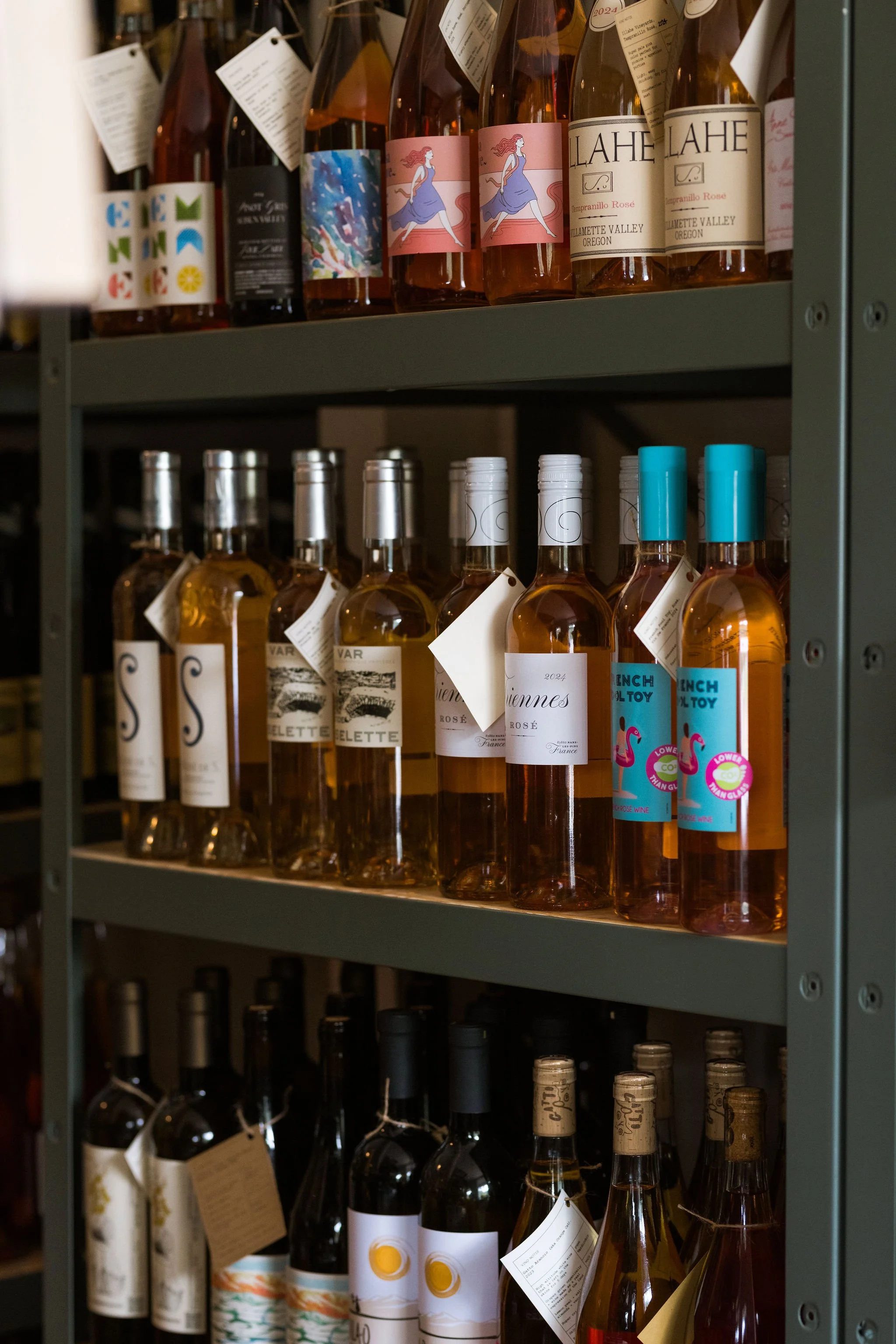 Shelves with various bottles of wine and rosé, some with colorful labels and tags.