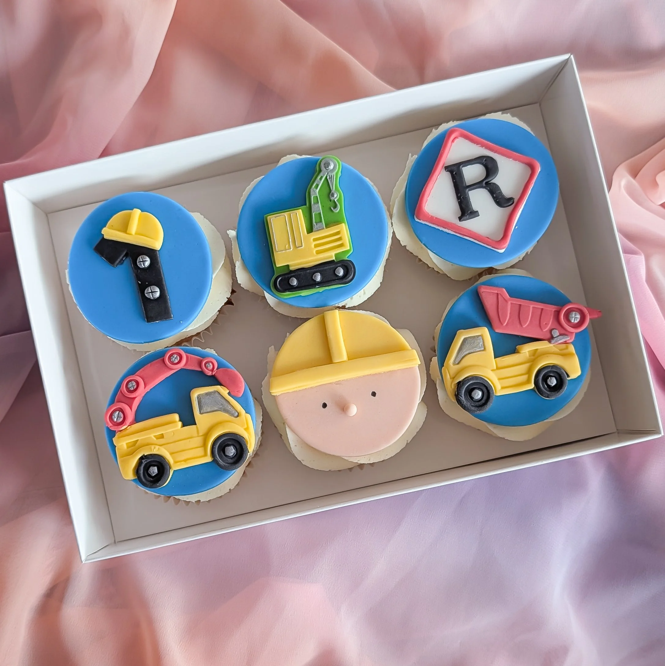 Decorative cookies in a box with construction-themed fondant toppers, including a yellow bulldozer, a green crane, and a red-and-black bulldozer.