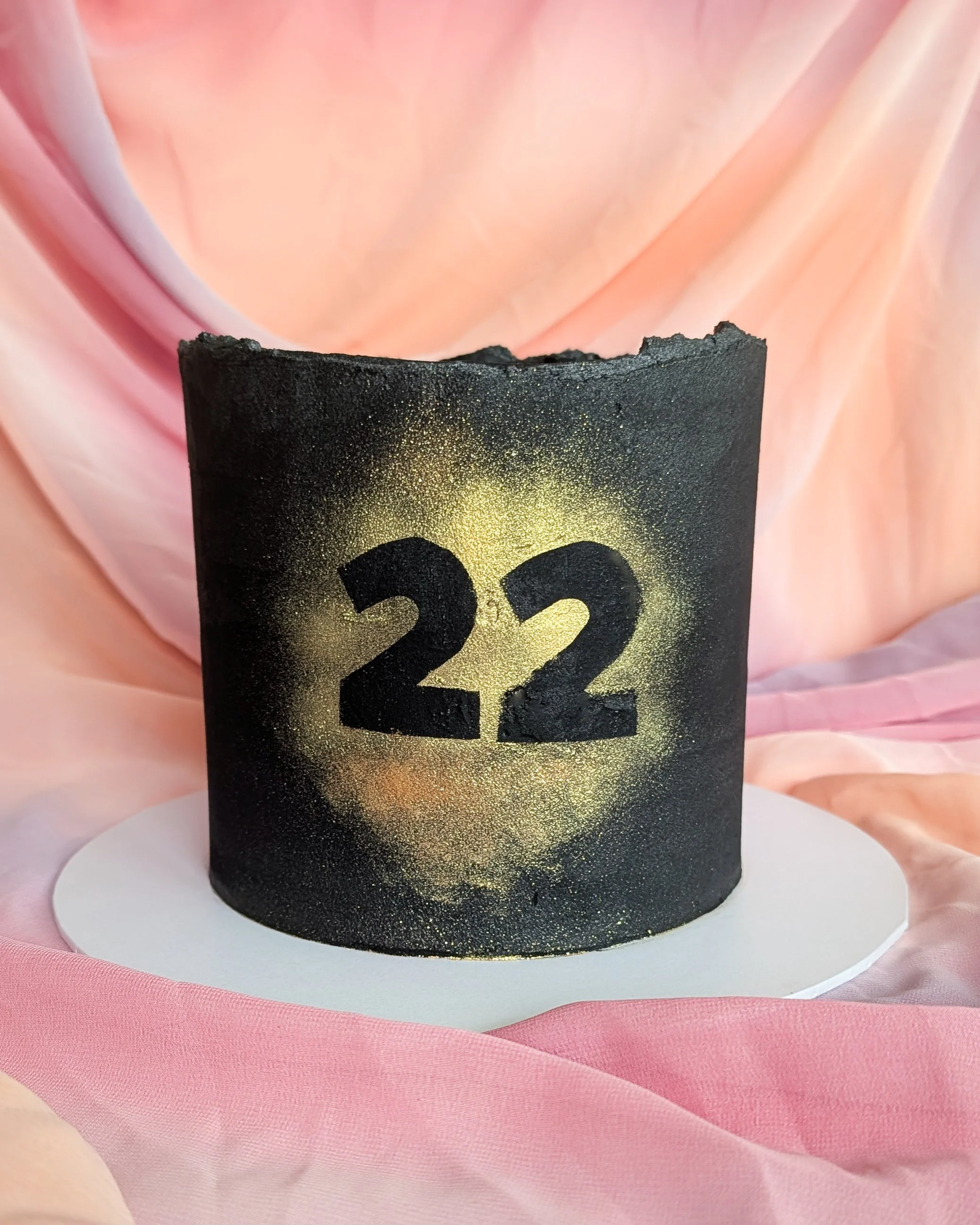 Close-up of a black birthday candle with the numbers 22 in gold, against pink and peach fabric background.