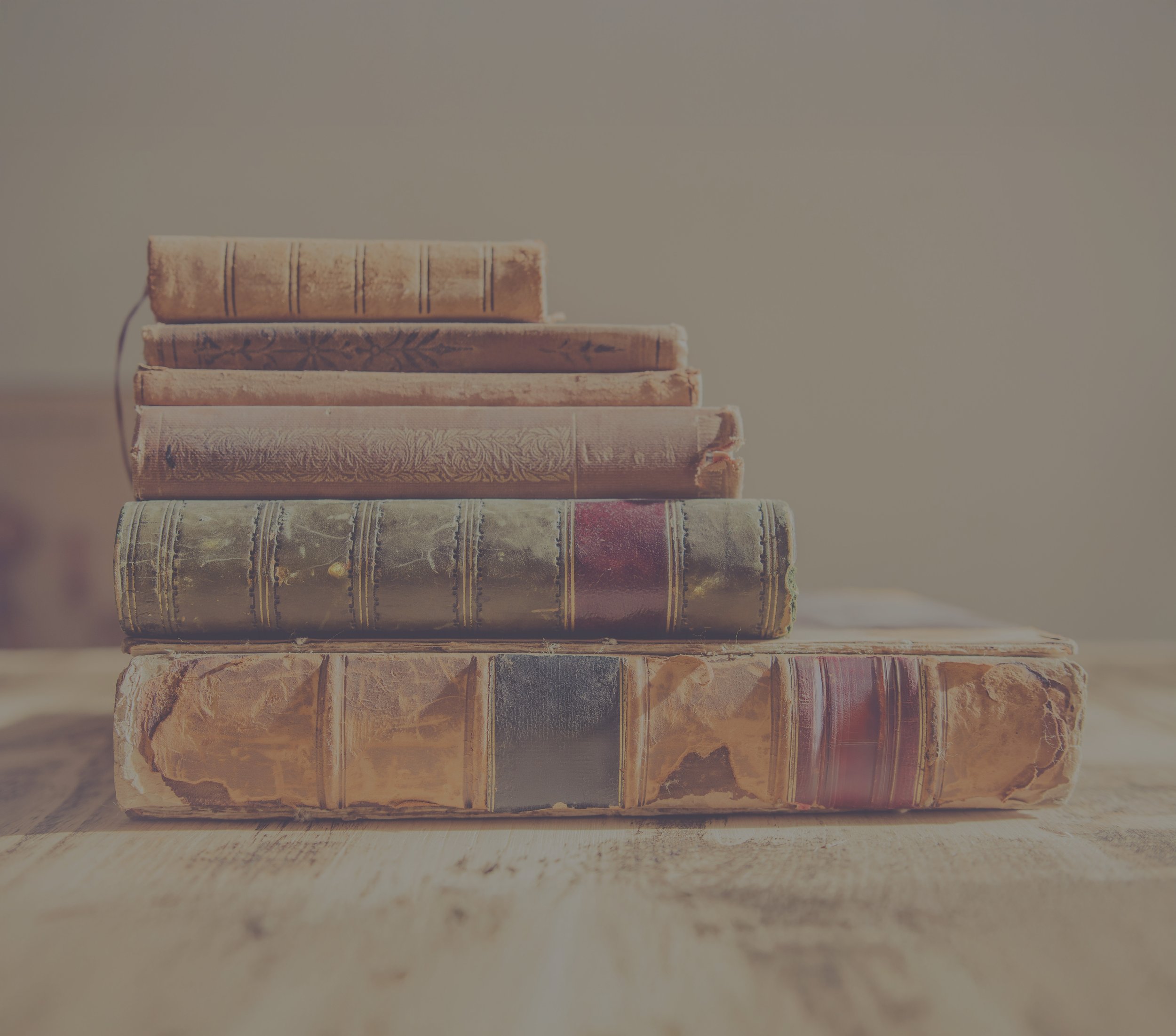 A stack of 6 vintage books on an old wooden table.