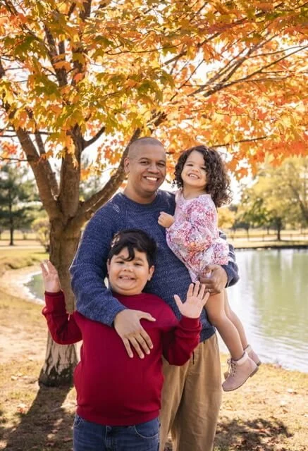 Sarah's husband, son, and daughter in front of a lake and tree in autumn.