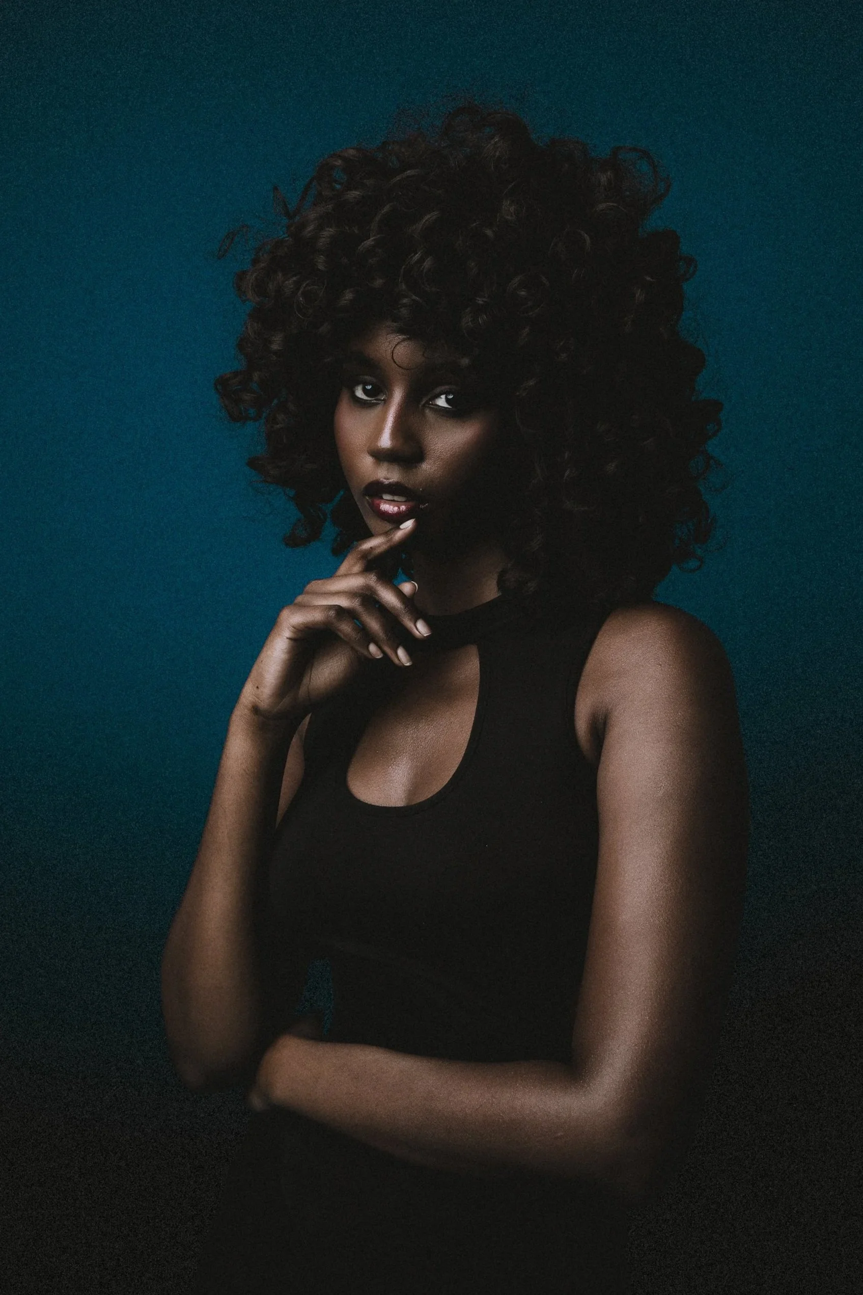 Portrait of a woman with curly hair wearing a black sleeveless top against a dark blue background.