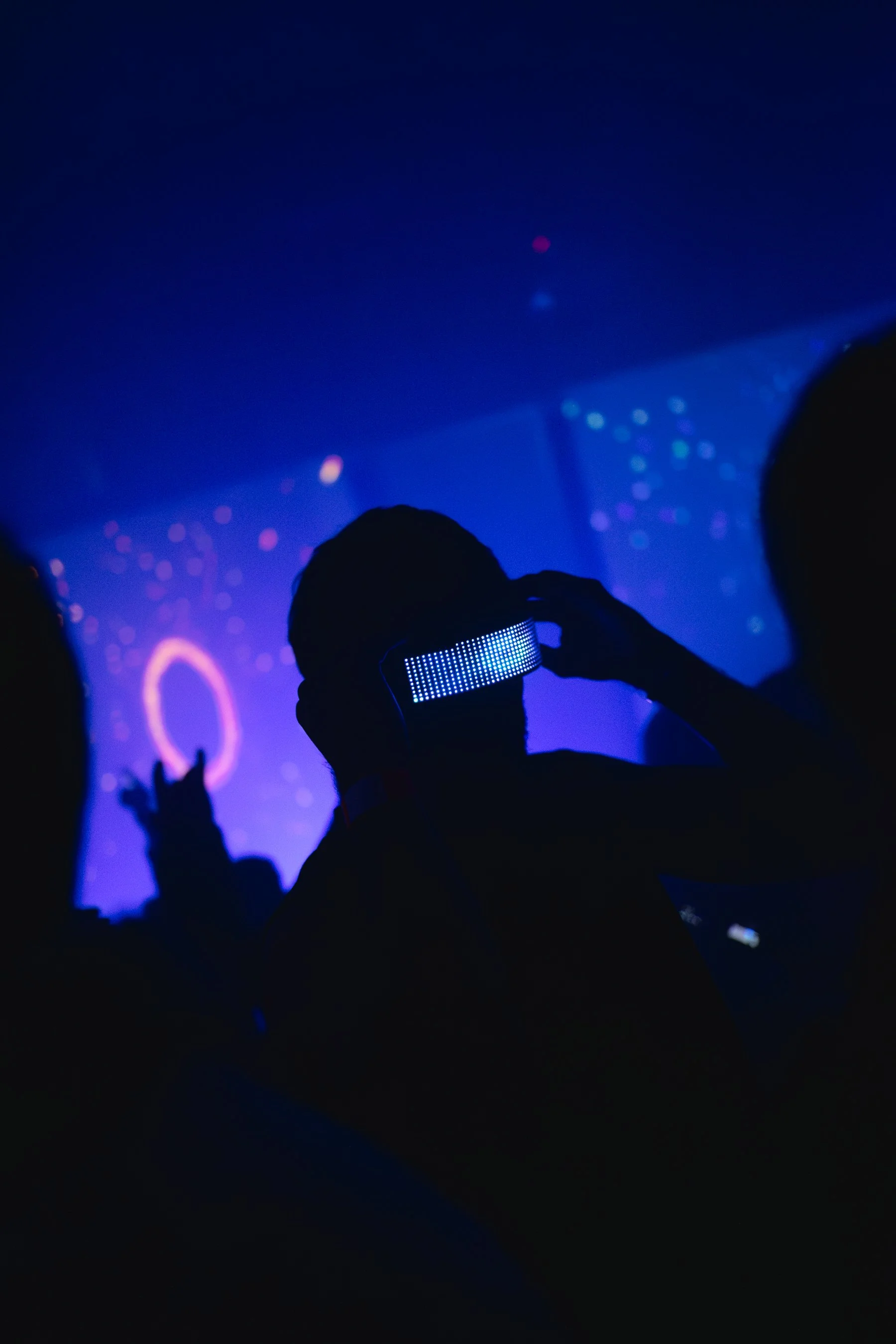 Person at a nightclub wearing a light-up LED mask, with colorful lights and abstract visuals in the background.