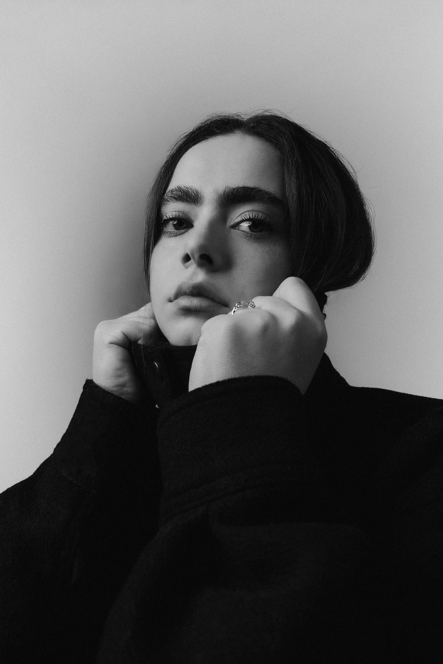 Black and white portrait of a woman with short hair, looking at the camera, resting her chin on her hand, wearing a dark top.