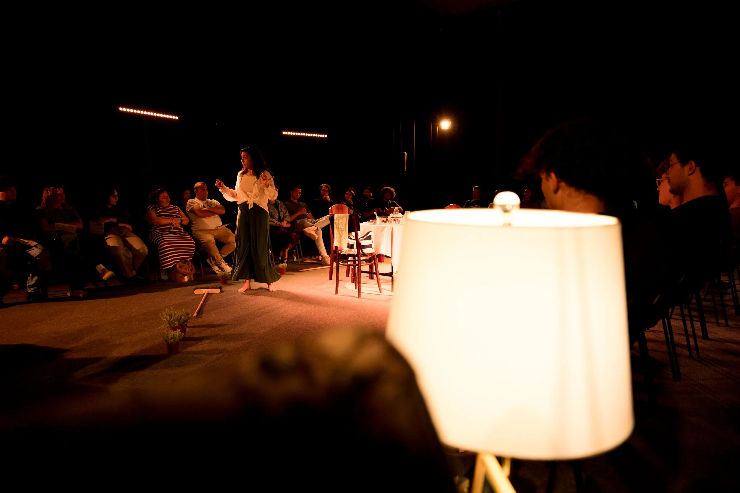 A woman performing on stage in front of an audience during a nighttime outdoor event, with audience members watching attentively.