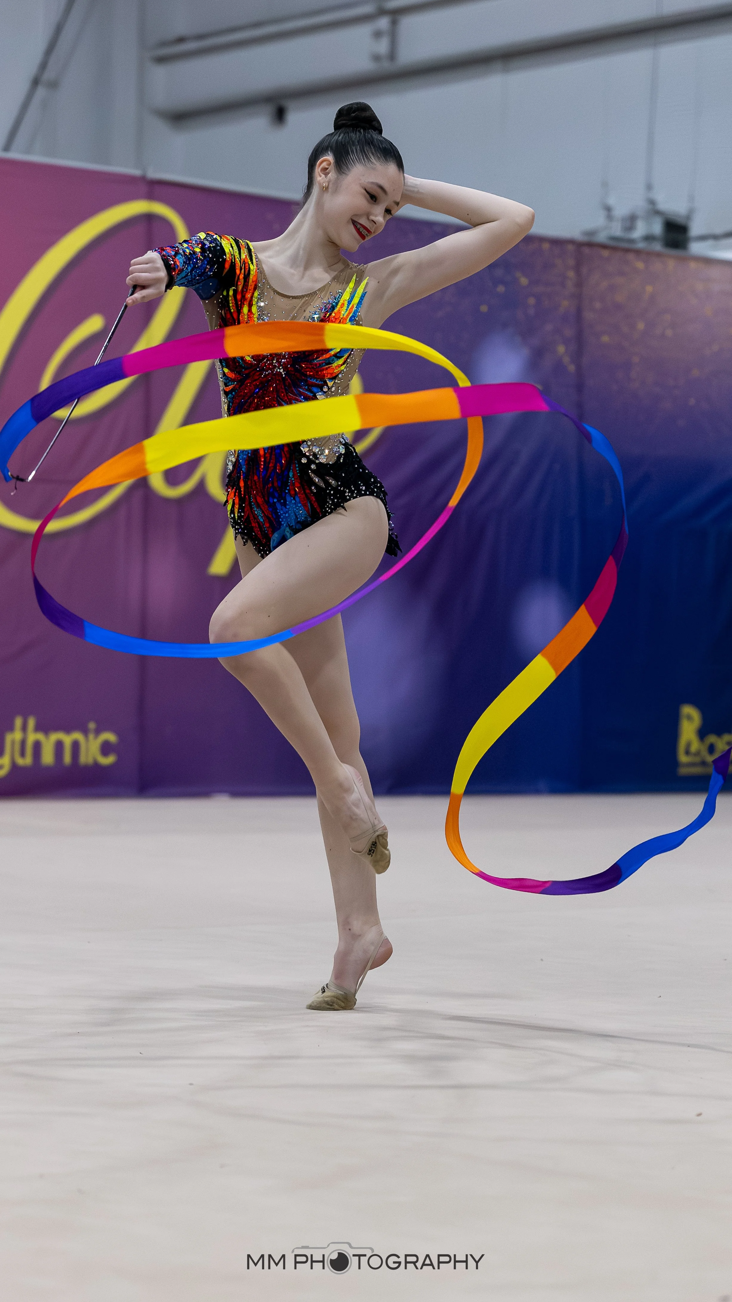 A rhythmic gymnast performing with colorful ribbons during a competition.