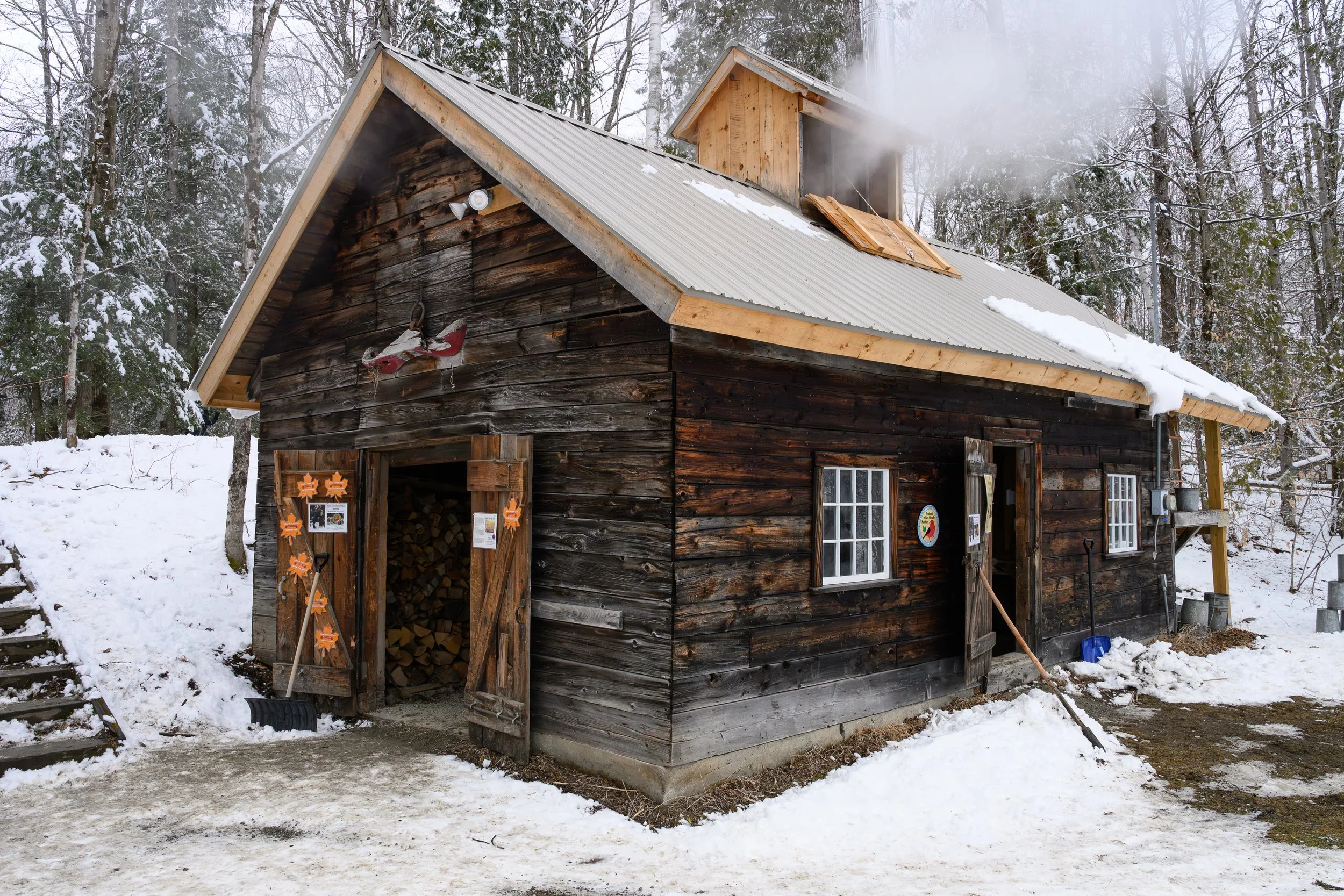 A wooden cabin with snow on the roof, surrounded by snow-covered trees in a winter forest.